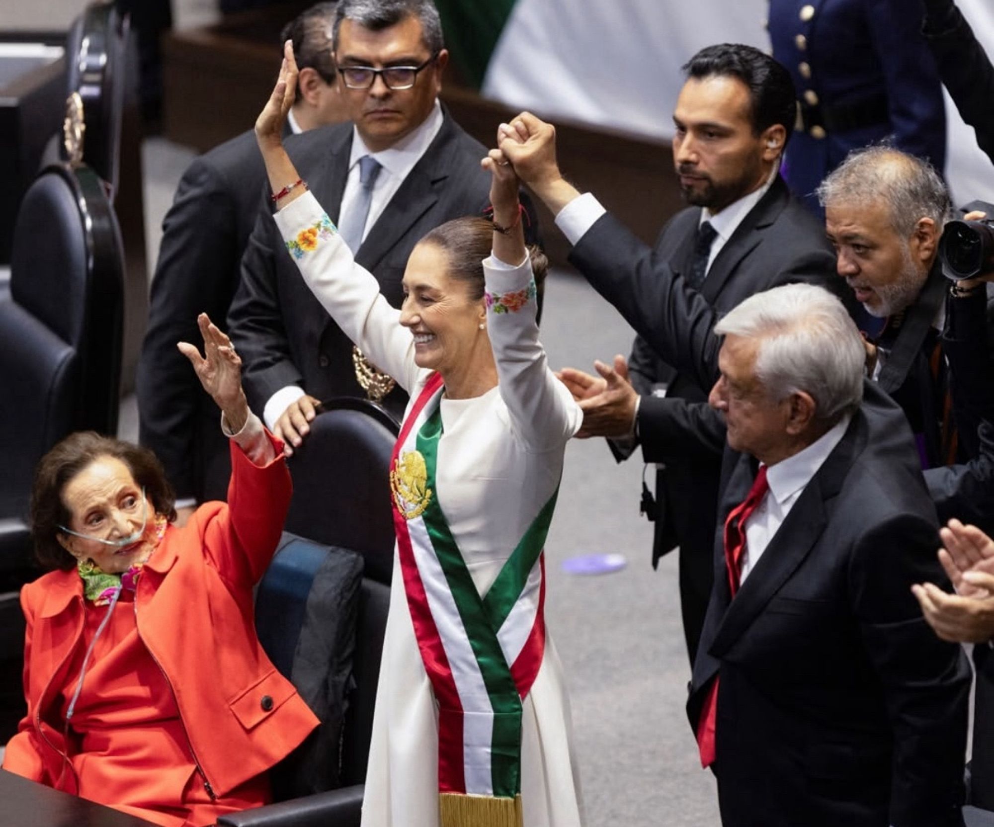 Claudia Sheinbaum surrounded by crowd of legislators, her arms raised to a welcoming crowd