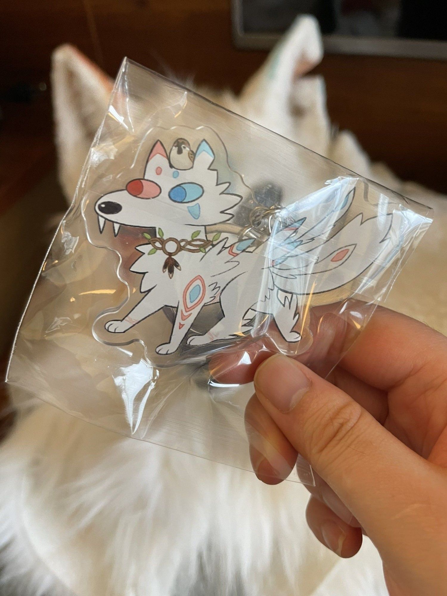 An acrylic charm of a Ary, a white wolf with a small sparrow on its head