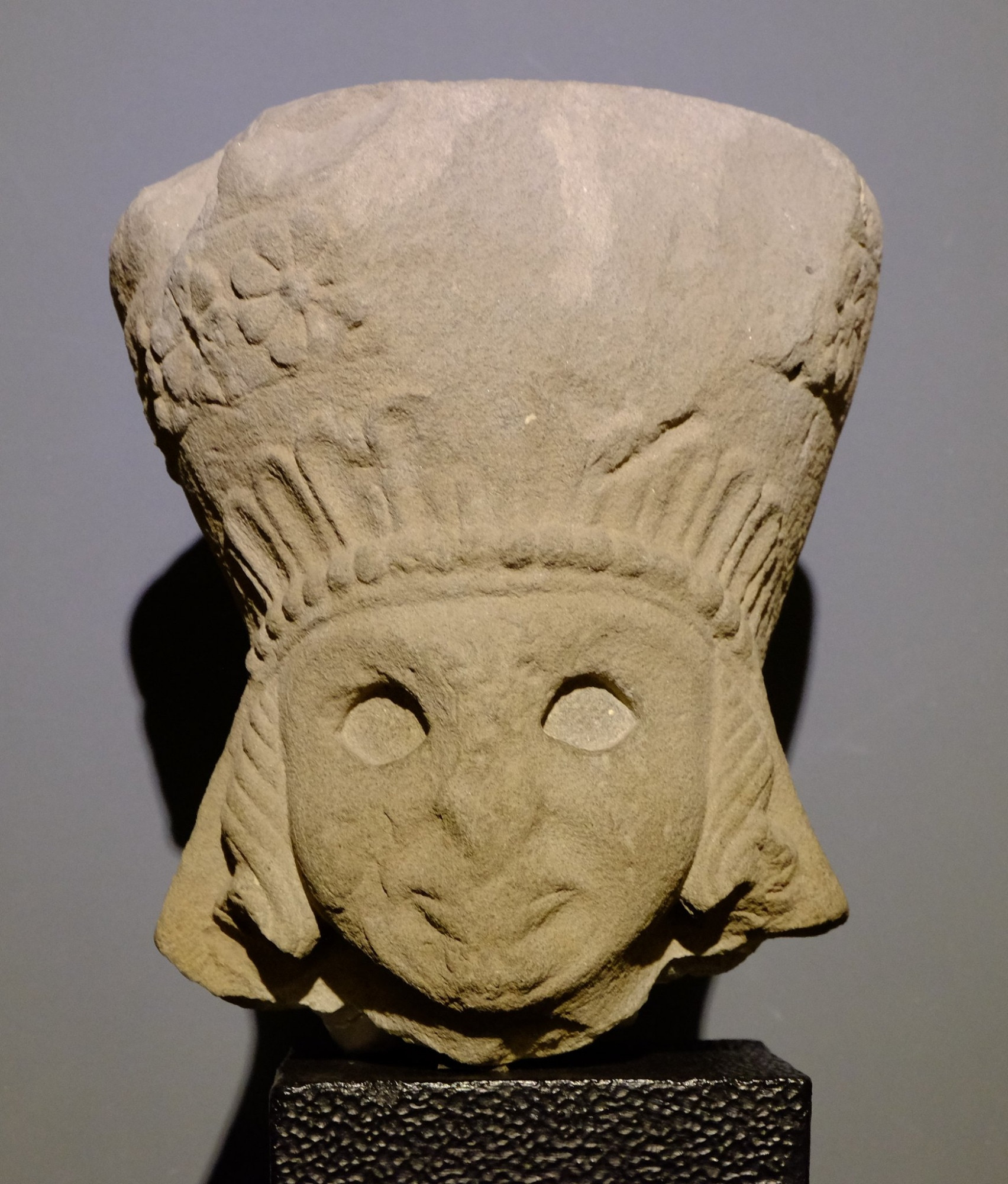 A sandstone sculpture of woman's head wearing a half-broken polos