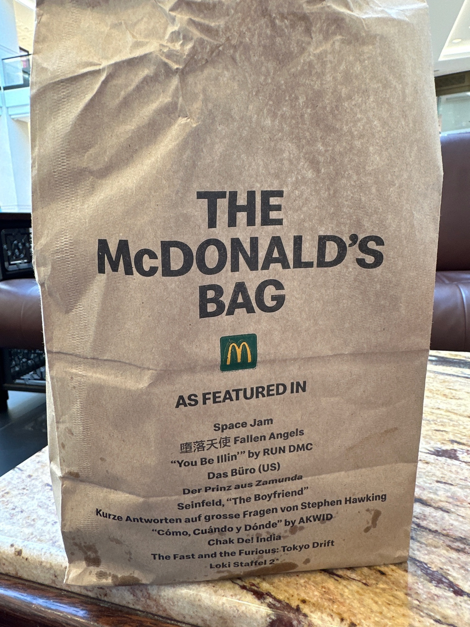 A brown paper McDonalds Bag that says “As Featured In” and then a mix of films and tv around the world, such as Space Jam and Seinfield.