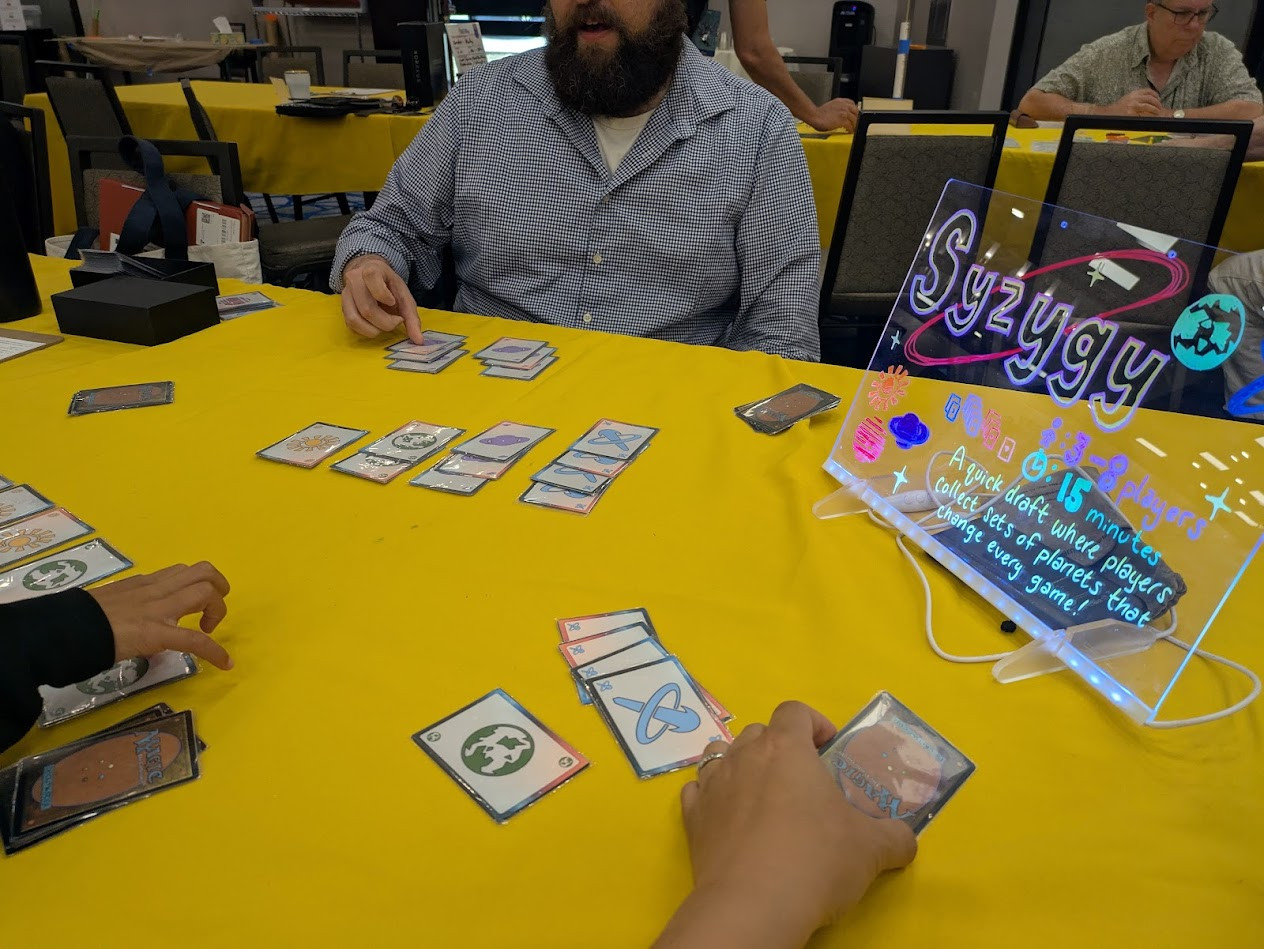 Lit up sign on the right side showing the name of the game and a description. On the table are cards grouped up by color/symbol.