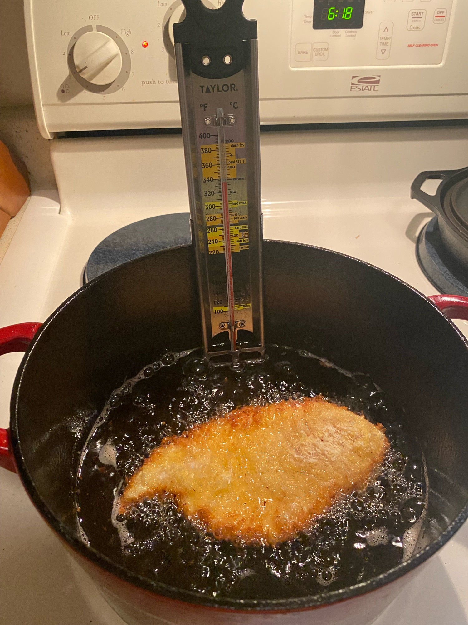 A breaded chicken cutlet is oil frying in a cast iron Dutch oven on a stovetop