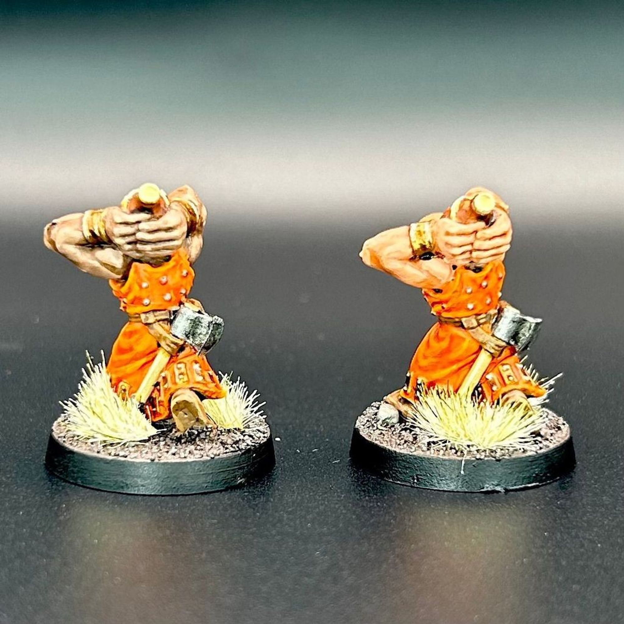 The backs of two dwarf scorcher miniatures from the Mordengard faction. They're bearded dwarfs with orange cloaks, throwing closed pots overhead. They have handaxes slung on their belts.