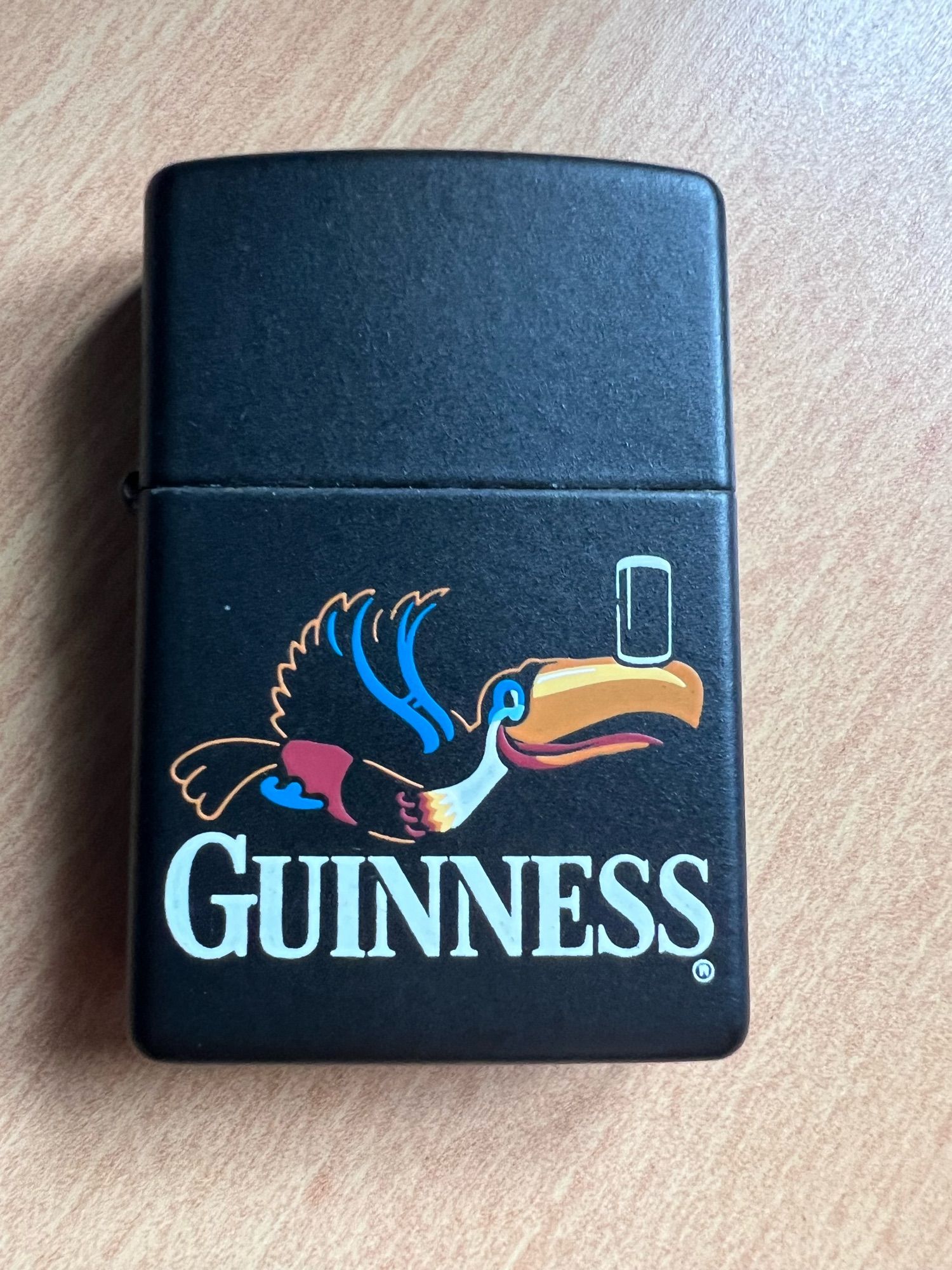 A Guinness branded Zippo lighter on a wooden desk.