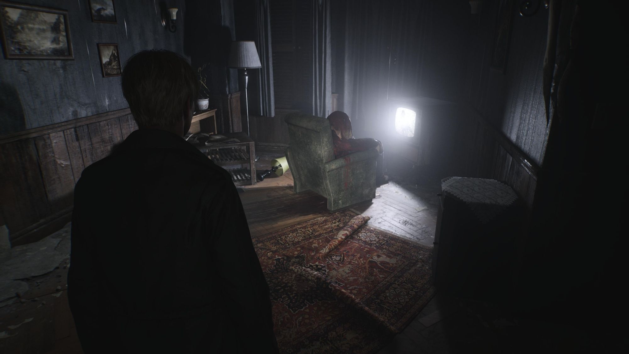 This is a screenshot from Bloober team's Silent Hill 2 remake on PS5. James Sunderland looks at a bloody shadow sat in front of a television set tuned to nothing but static. Light streams from the television set, casting long shadows around the room.