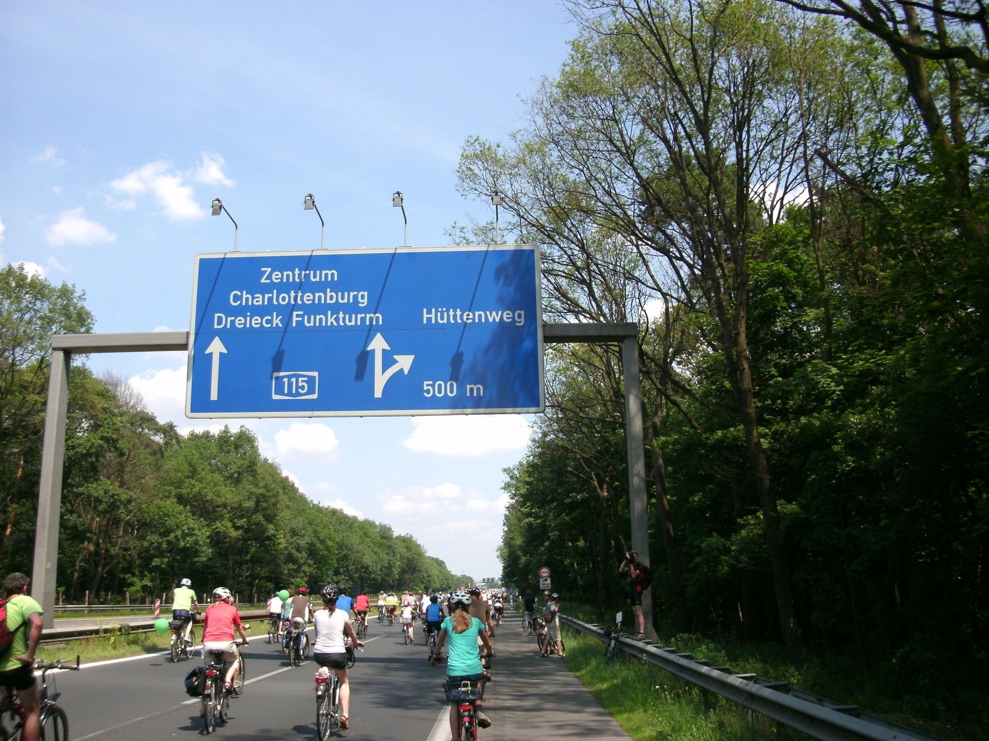 Bild von Juni 2015. Fahrradfahrende auf der Autobahn unter einem blauen Autobahnhinweis. Geradeaus Zentrum, Charlottenburg, Dreieck Funkturm. Rechts nach Hüttenweg