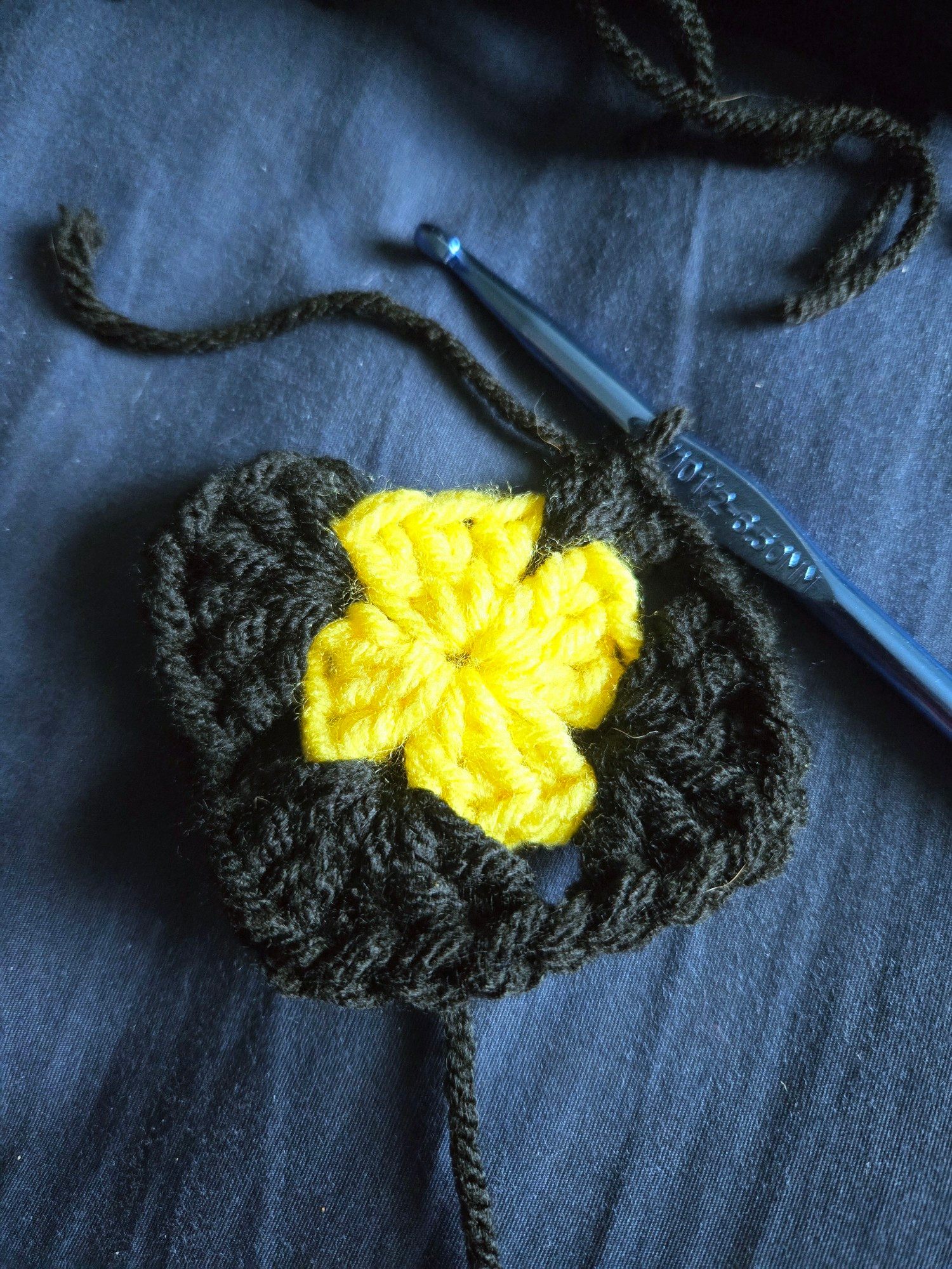 An unfinished yellow and black granny square.