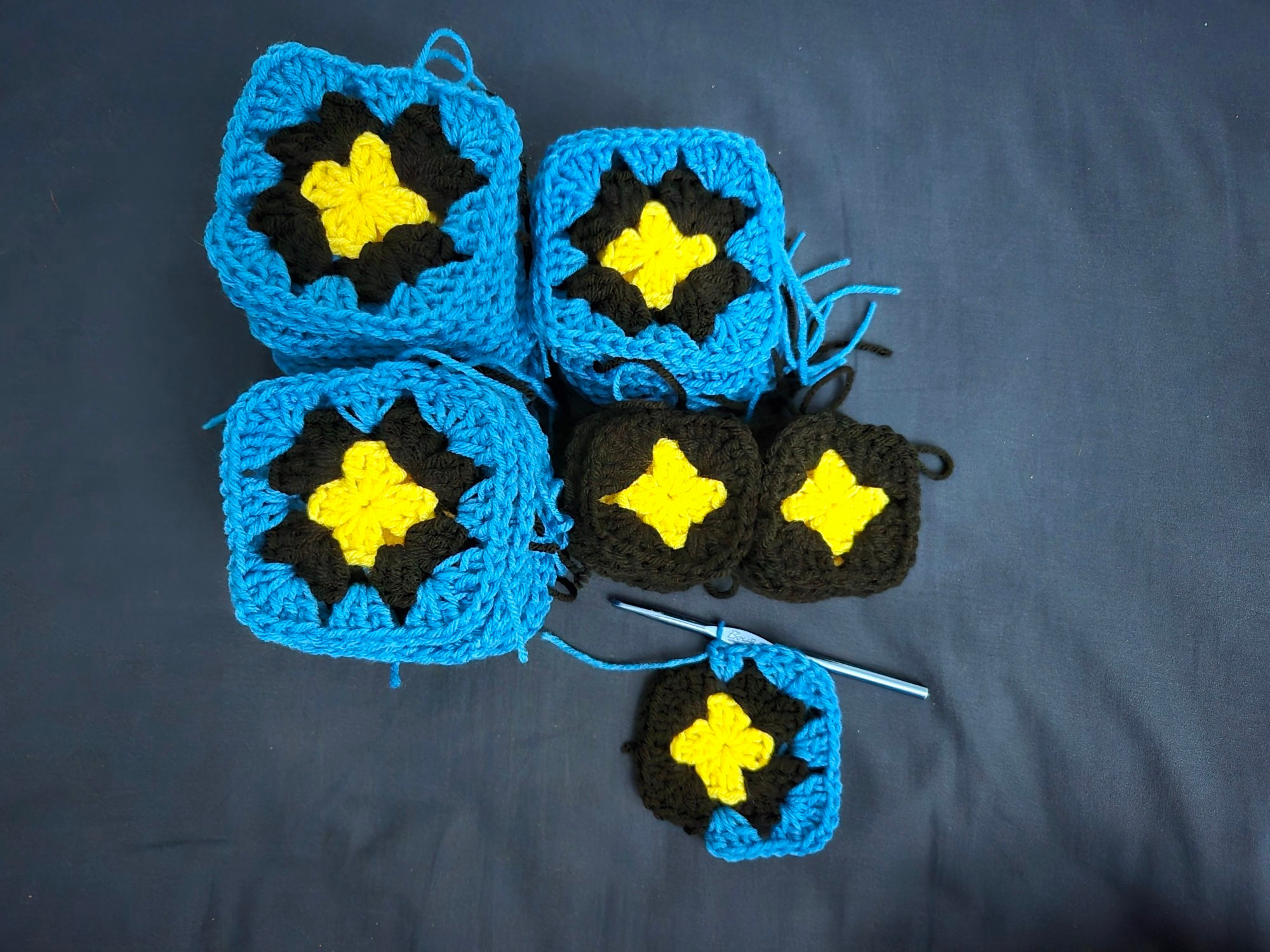 Piles of granny squares. Some are yellow, black, and blue, others are only yellow and black.