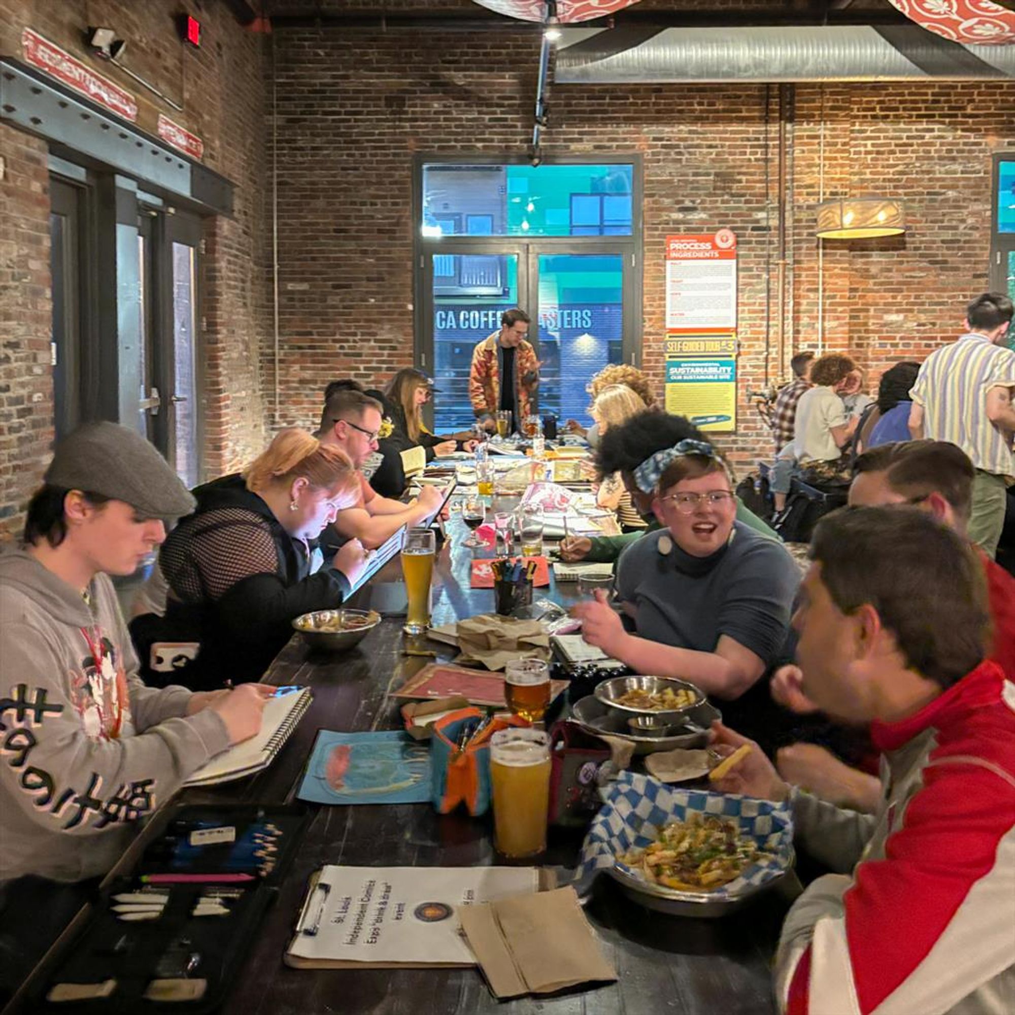 Group of people at a long table chat, laugh, and draw.