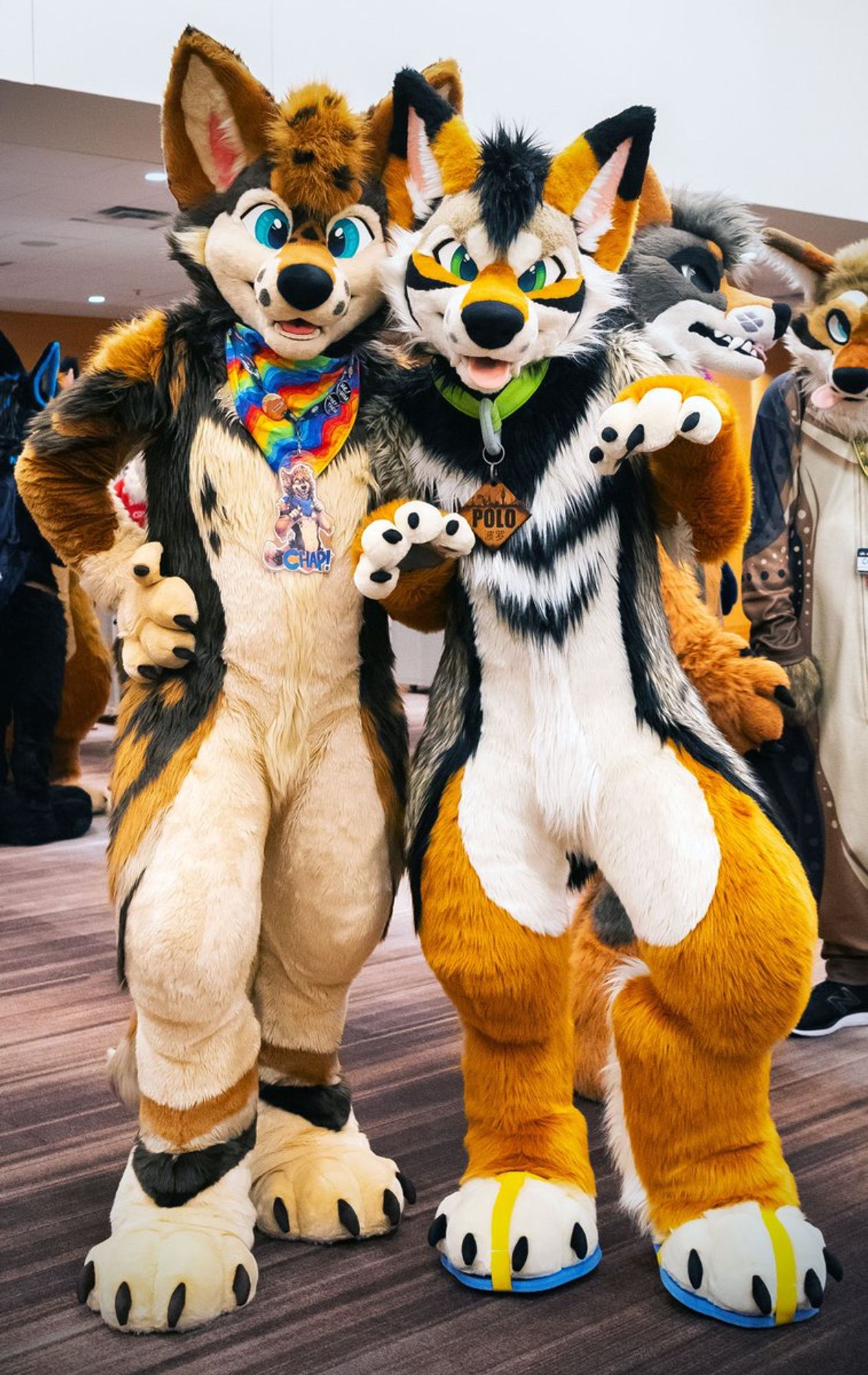 Two coyote fursuiters standing side by side, one with a friendly expression and the other with a more mischievous look