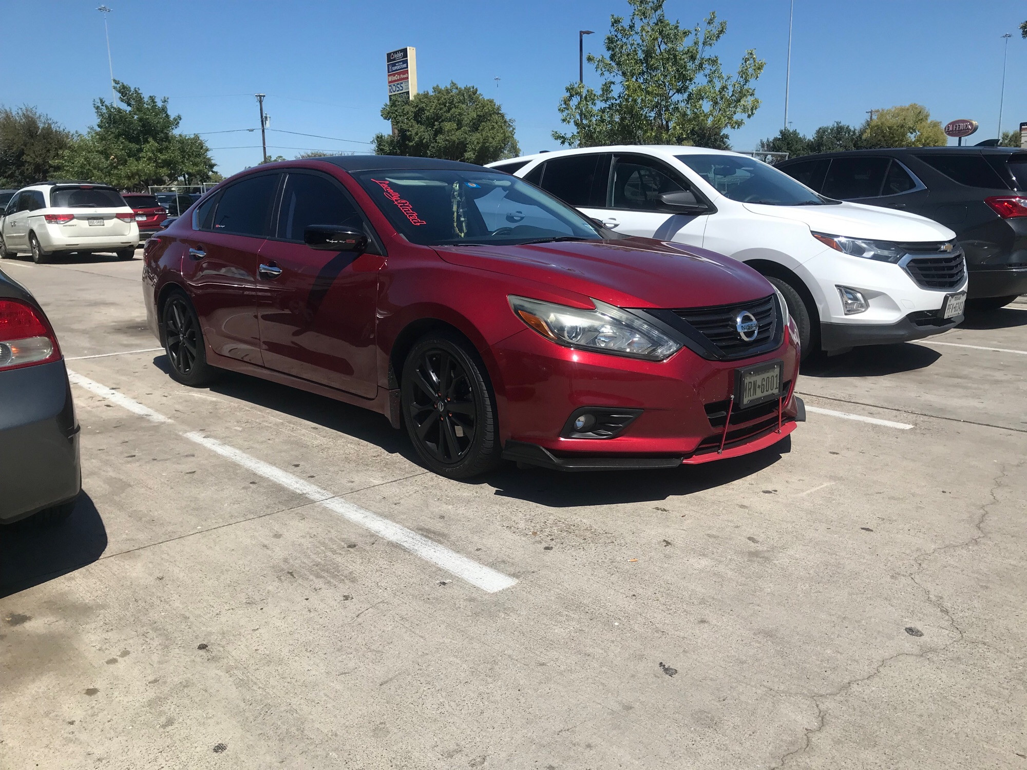 A red Nissan Altima SR trim strim with front splitter, carbon fiber effect window trim and gloss black paint wheels, mirrors, and spoiler