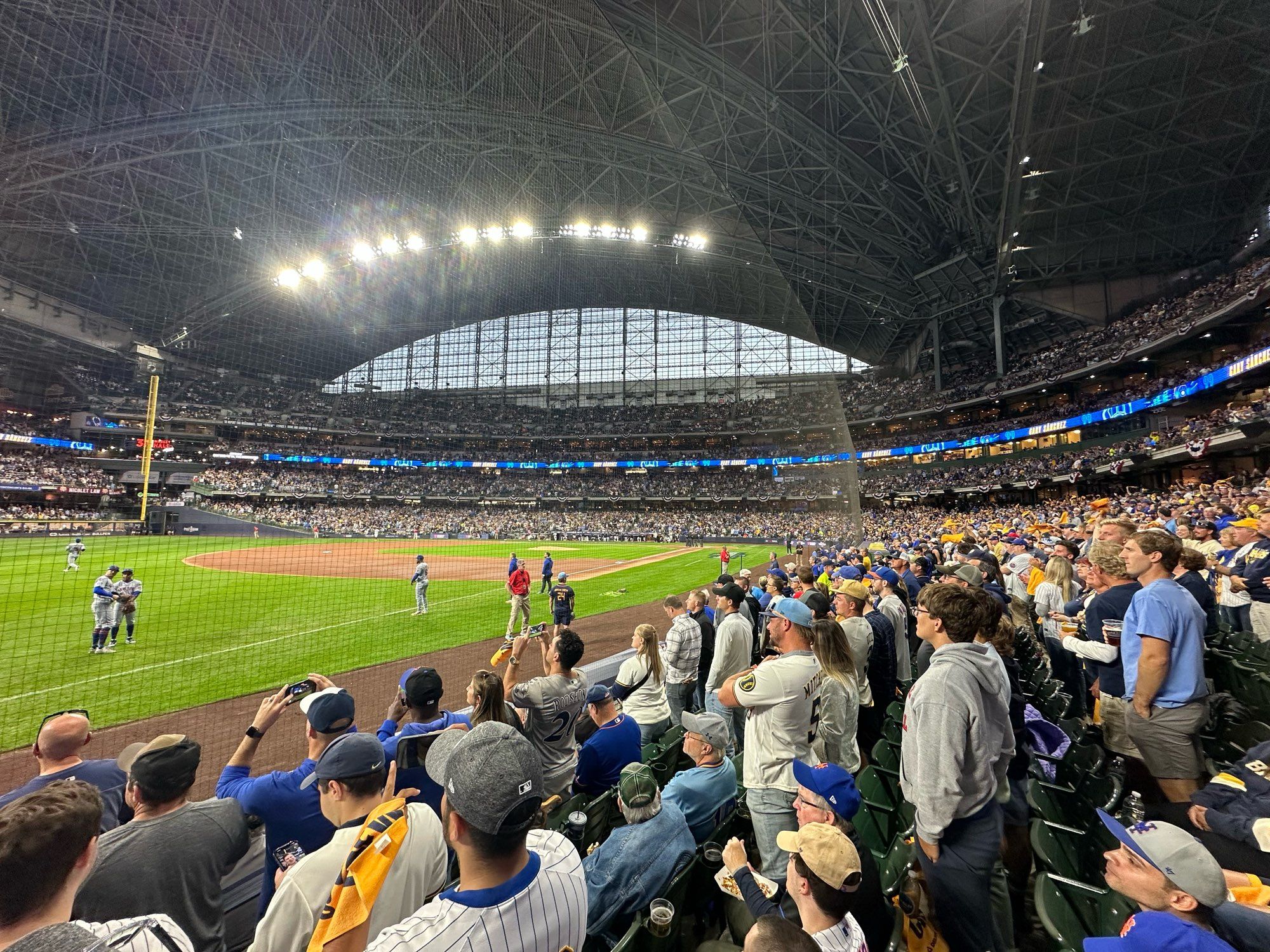 Wife angle picture of MLB NL WCS game Mets at Brewers. Looking in from third base/shallow left field across diamond with right field foul pole at left and home play at right. Fans standing waiting for game to start.