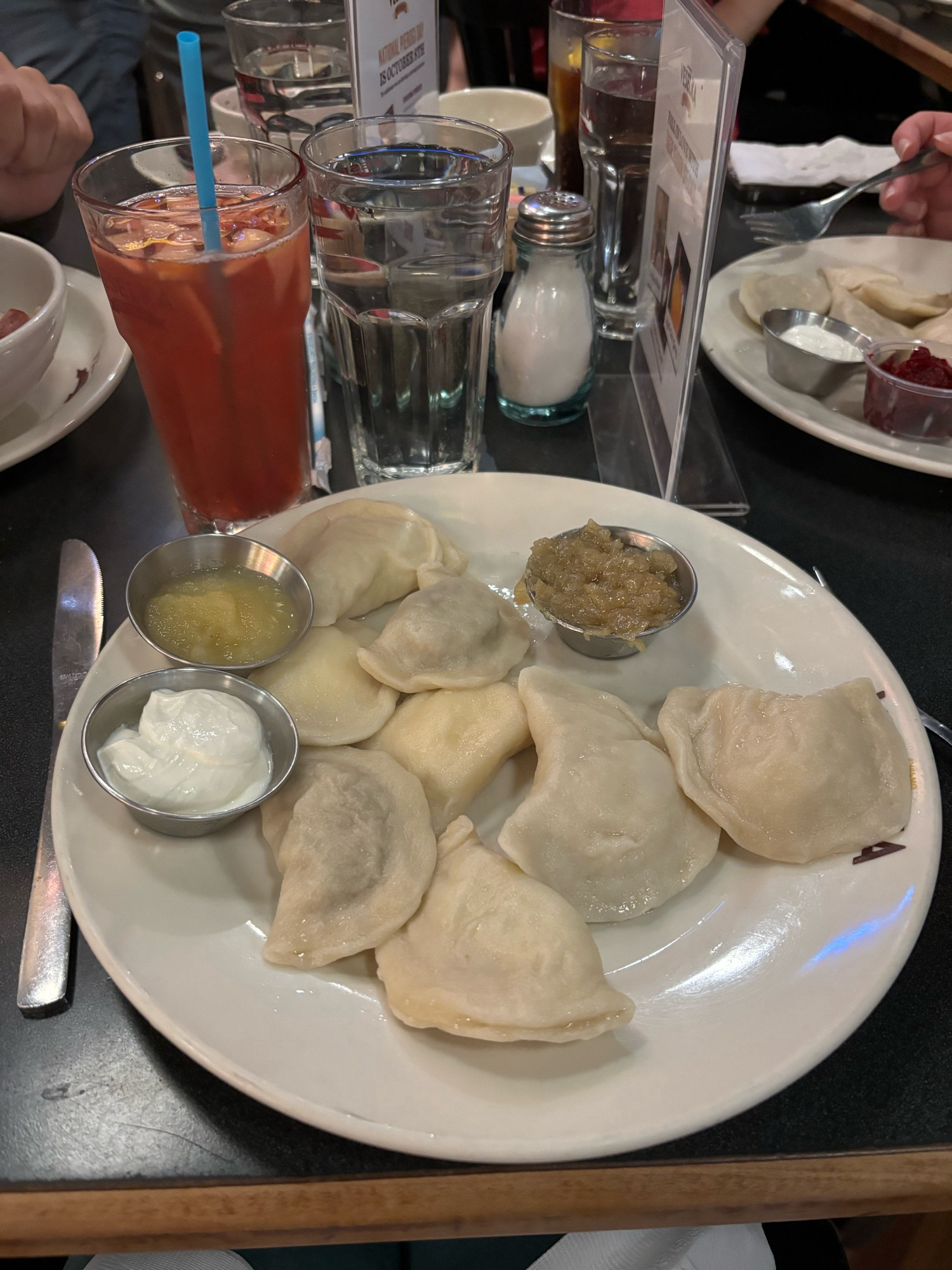 A plate of 8 pierogis with sour cream, applesauce and sautéed onions with a red drink