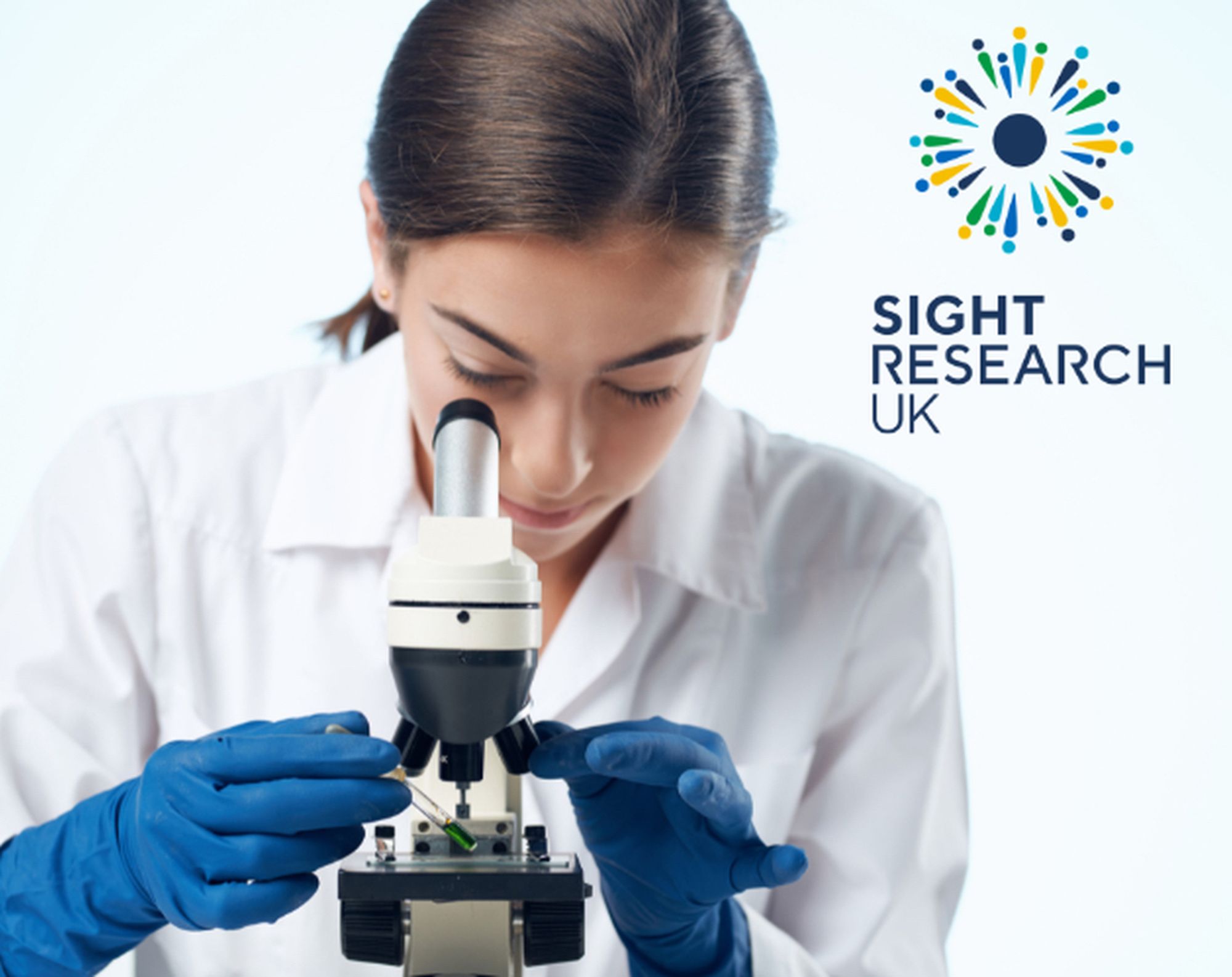 Person in a lab coat looking through a microscope. Sight Research UK charity logo in the top right corner of image.