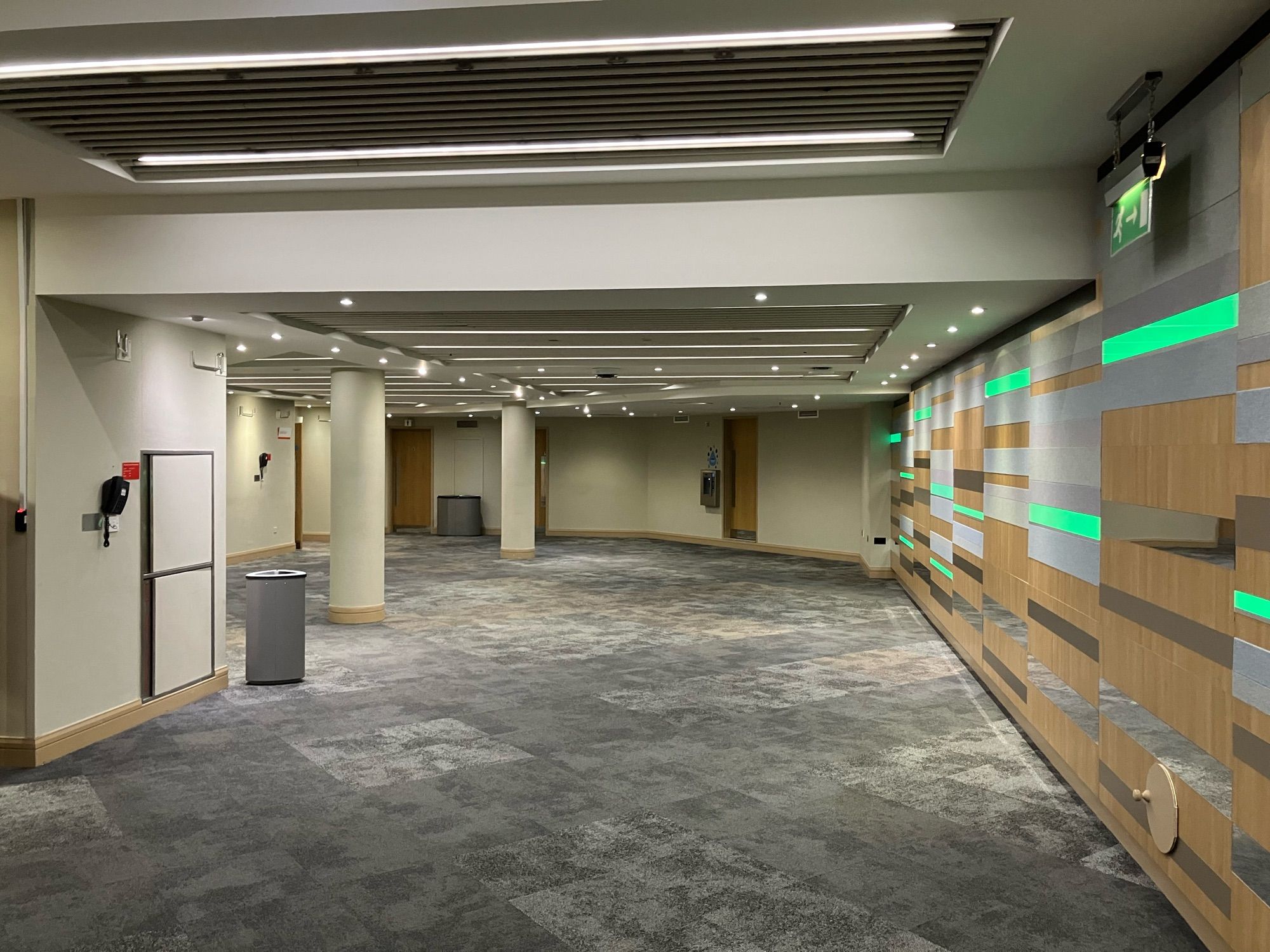 An empty corridor with grey carpet, white pillars and grey, brown and green panelling on the wall