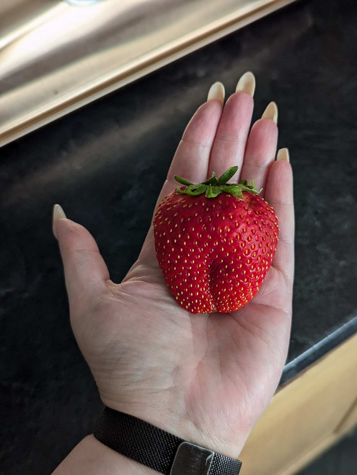 My open hand holding a chonky strawberry that is almost as big as my palm.