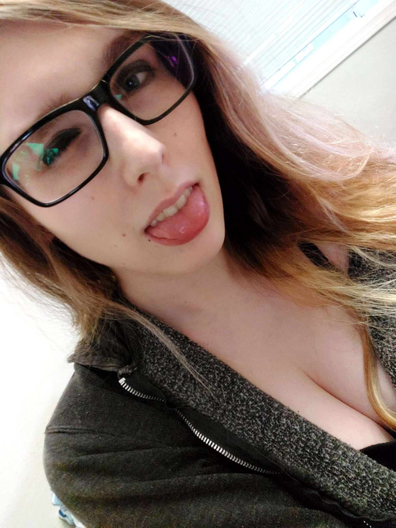 Tongue out blonde lady with a hoodie and thick glasses. She might think she's cute idk