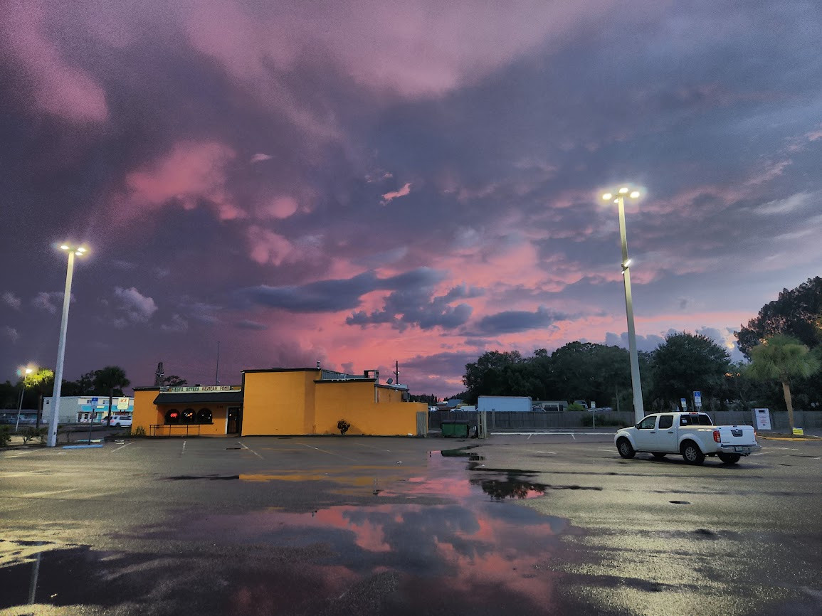 Parking lot with a large puddle reflecting the pink and purple of the sky at dusk after a storm