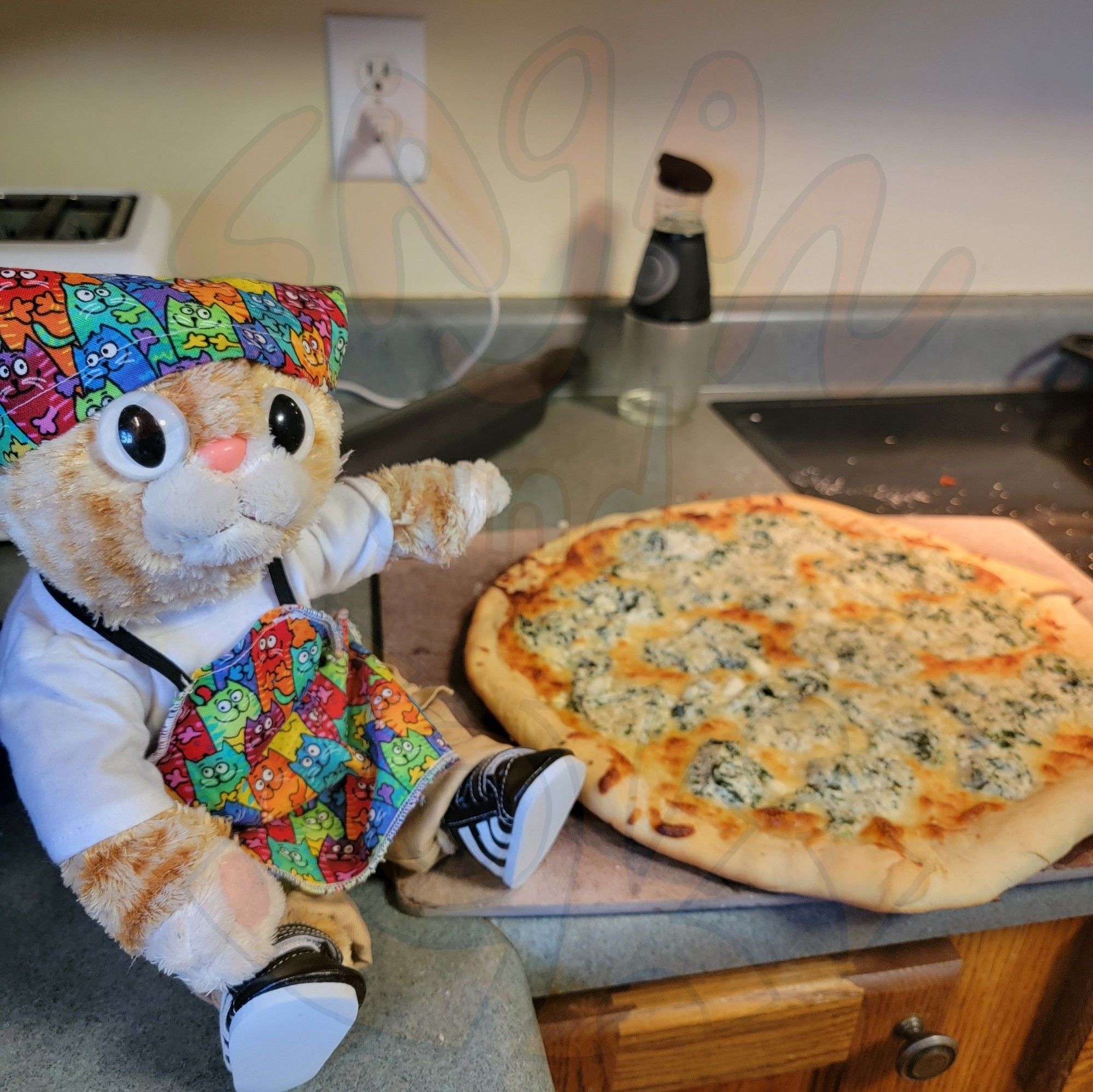 An orange plush cat in a colorful apron and bandana shows off his spinach pizza.