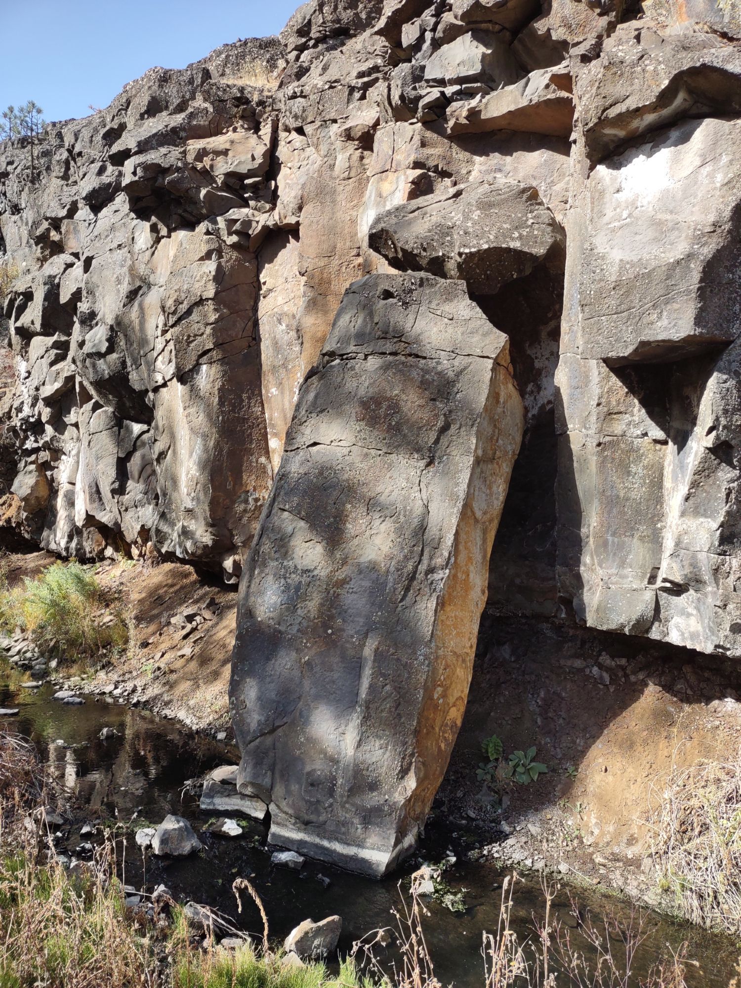 A large rectangular sized rock dismantled from a rocky hillside by a creek.