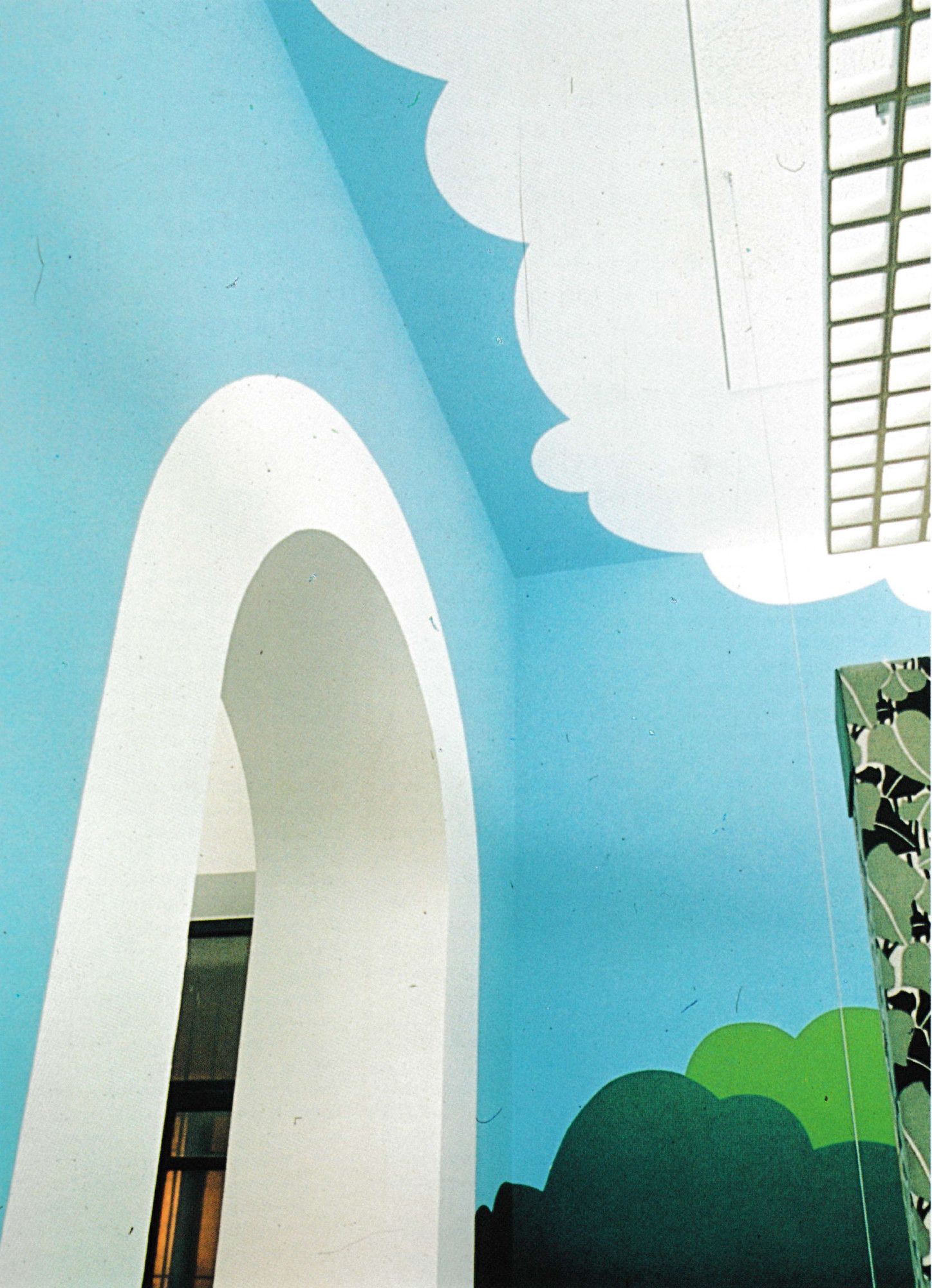 Shot looking up at a white arched doorway in a sky-blue room. A cartoon cloud painted on the ceiling wraps slightly onto the far wall, above some similarly abstracted green trees.