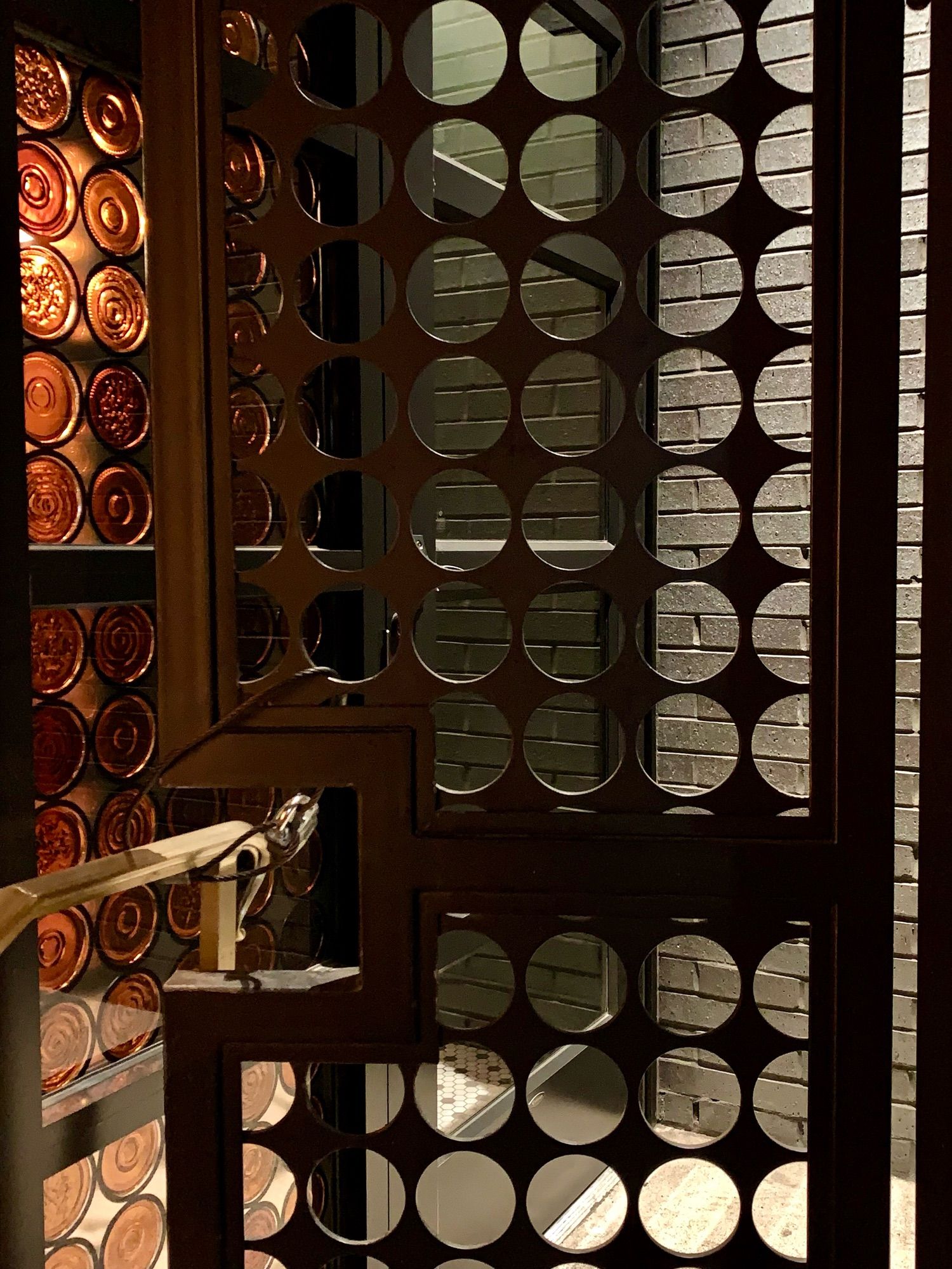 Beautifully detailed entryway featuring a panel of circles cut from steel, leading to another door with circles made of glass in golden bronze tone - Printers Alley - Nashville, Tennessee