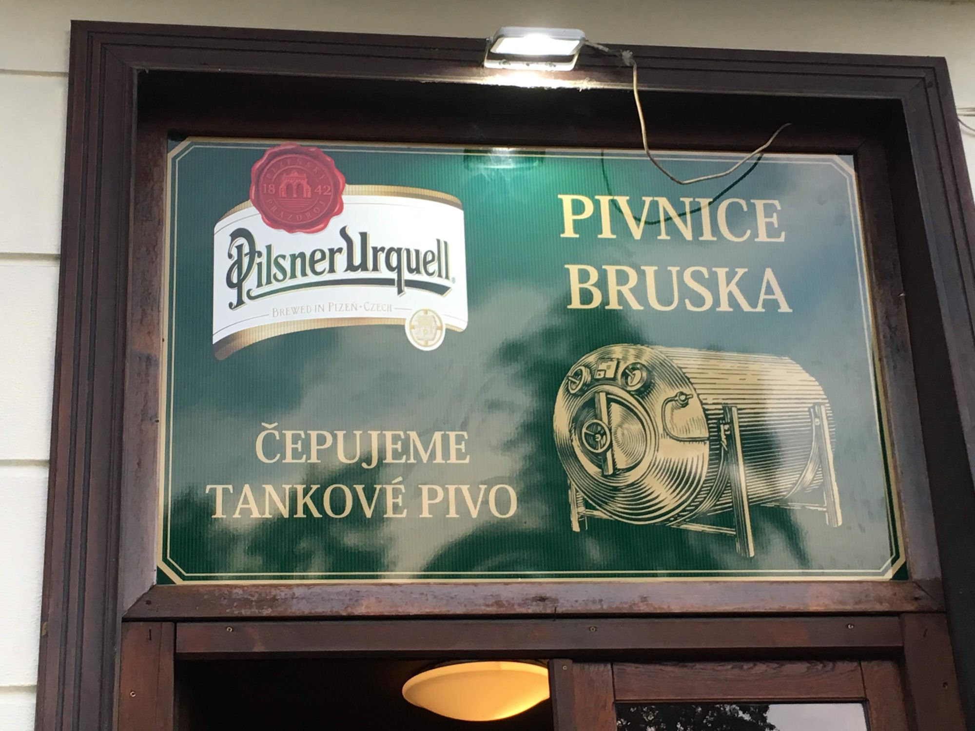 a sign for a Prague Pilsner Urquell chain pub (here in Dejvice quarter of Prague) with typical gold lettering on green ground to match the beer label, with an image of the long beer tank