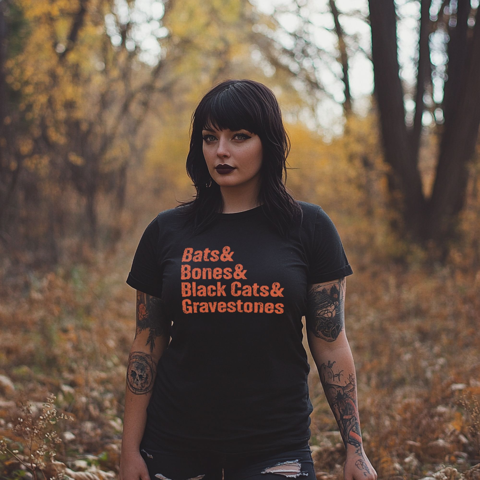 A tattooed goth-looking woman wearing a black t-shirt that reads "Bats & Bones & Black Cats & Gravestones" in orange text.