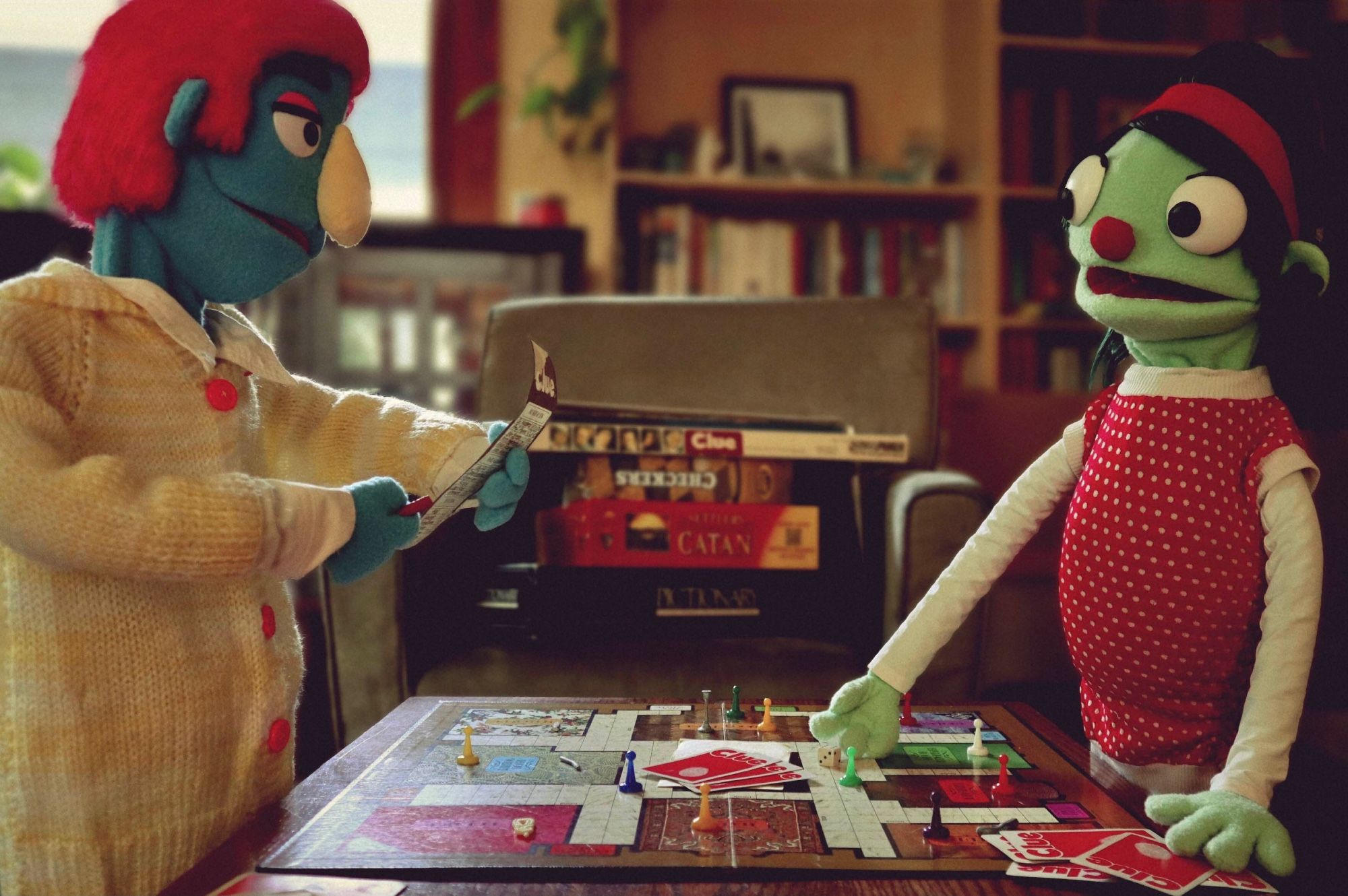 Two puppets playing clue. One has blue skin and pink hair and the other has green skin and hair. 