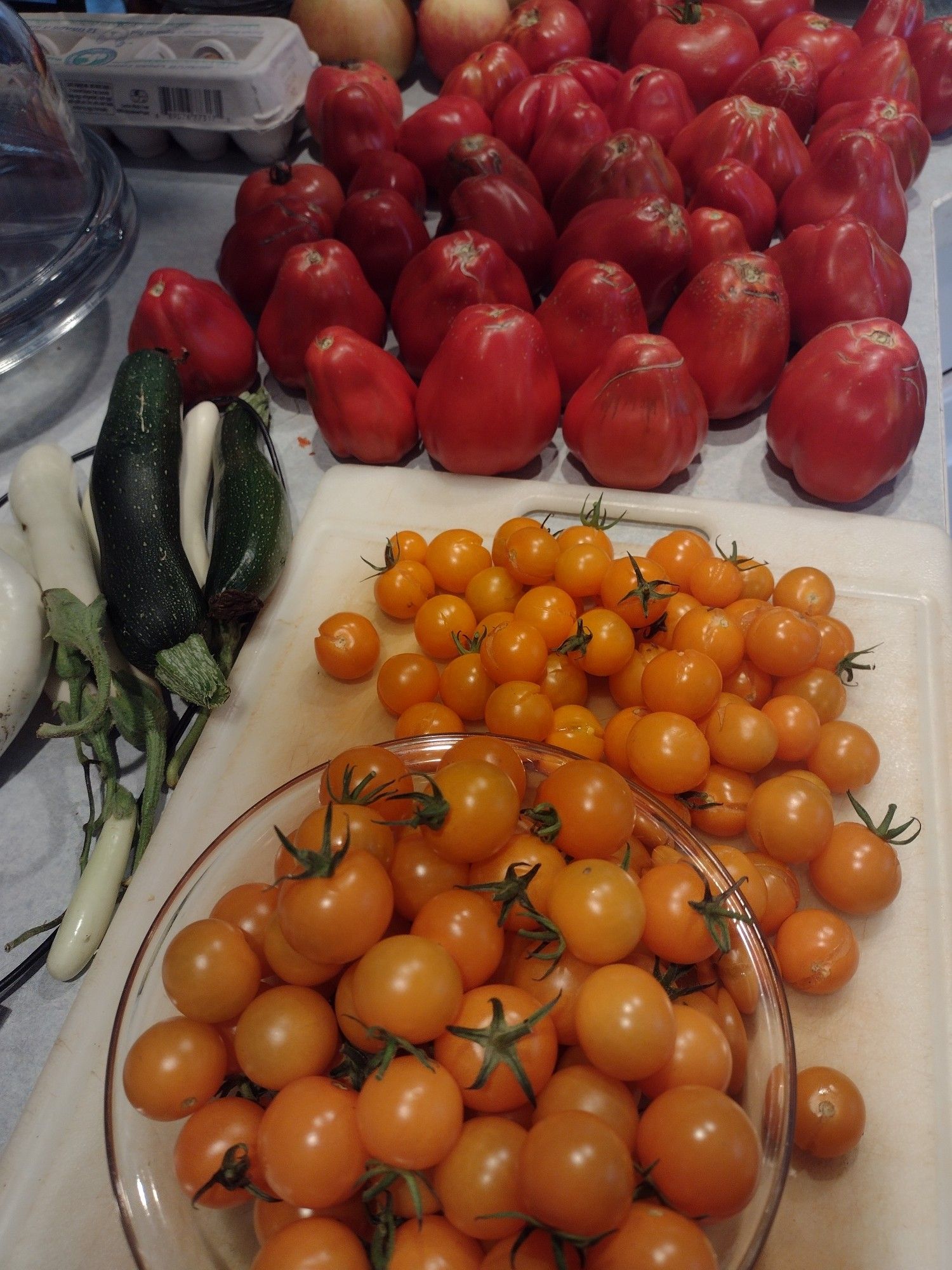 A counter full of orange and red garden tomatoes with a few white eggplant and green zucchini on the side