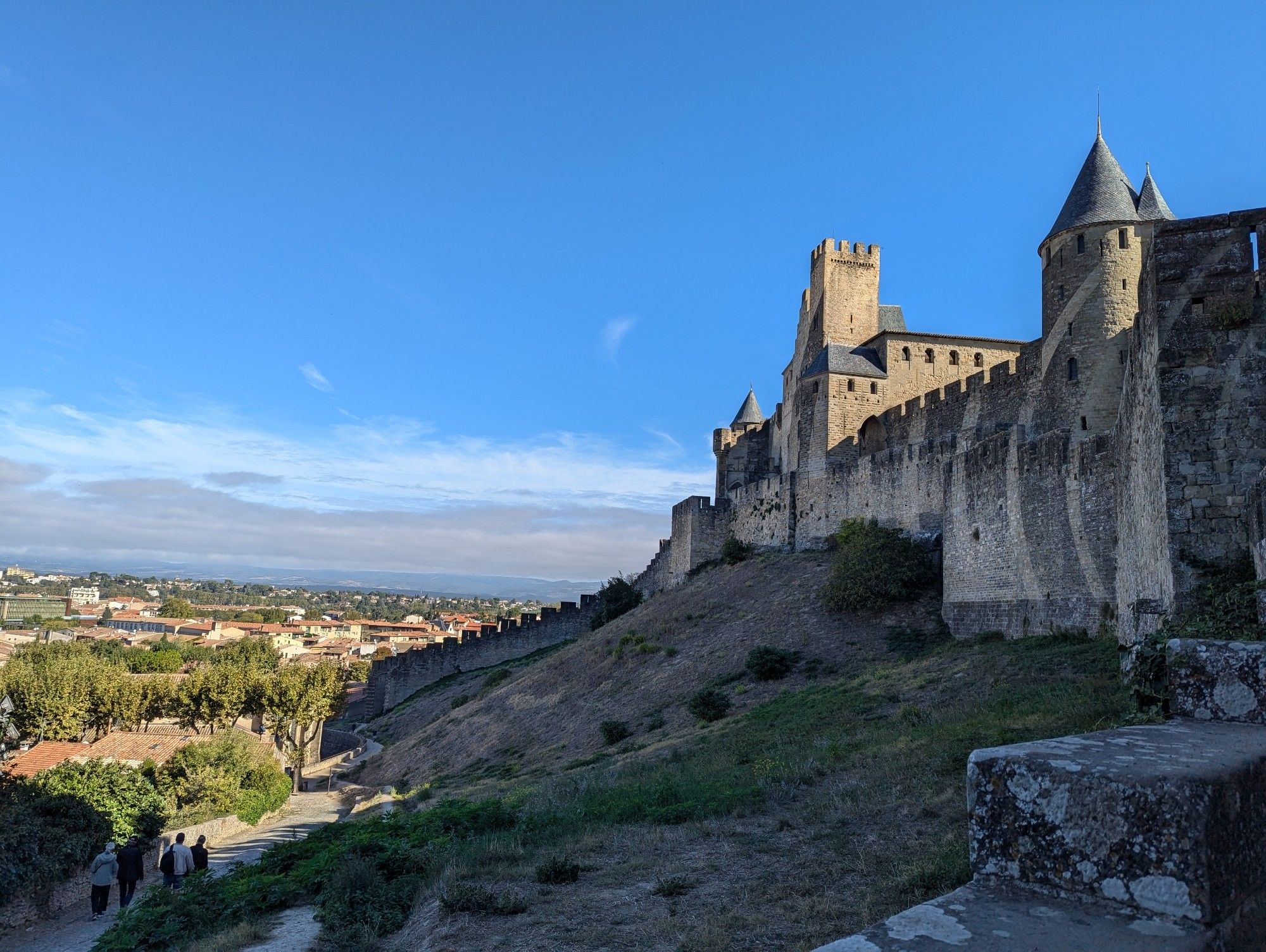 On the right are towers, turrets and walls of stone, down the hill to the left are the red roof tiles of the main old town of Carcassonne