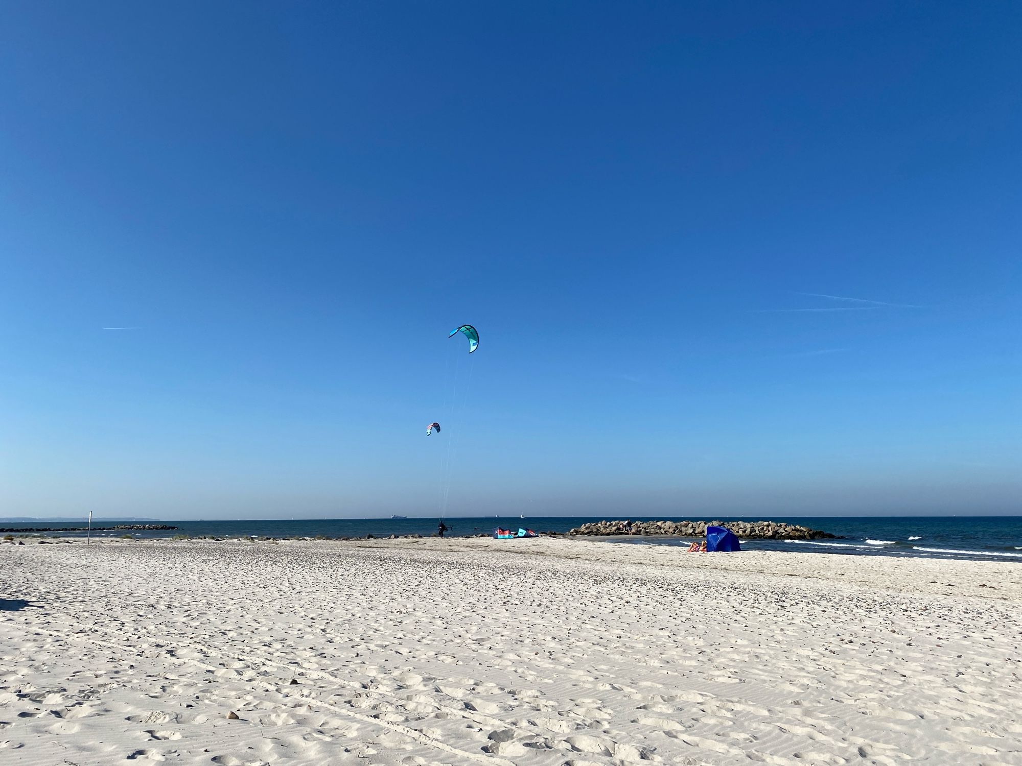 Strand, entfernt ein Kitesurfer, blauer Himmel und ein schmaler Streifen Ostsee