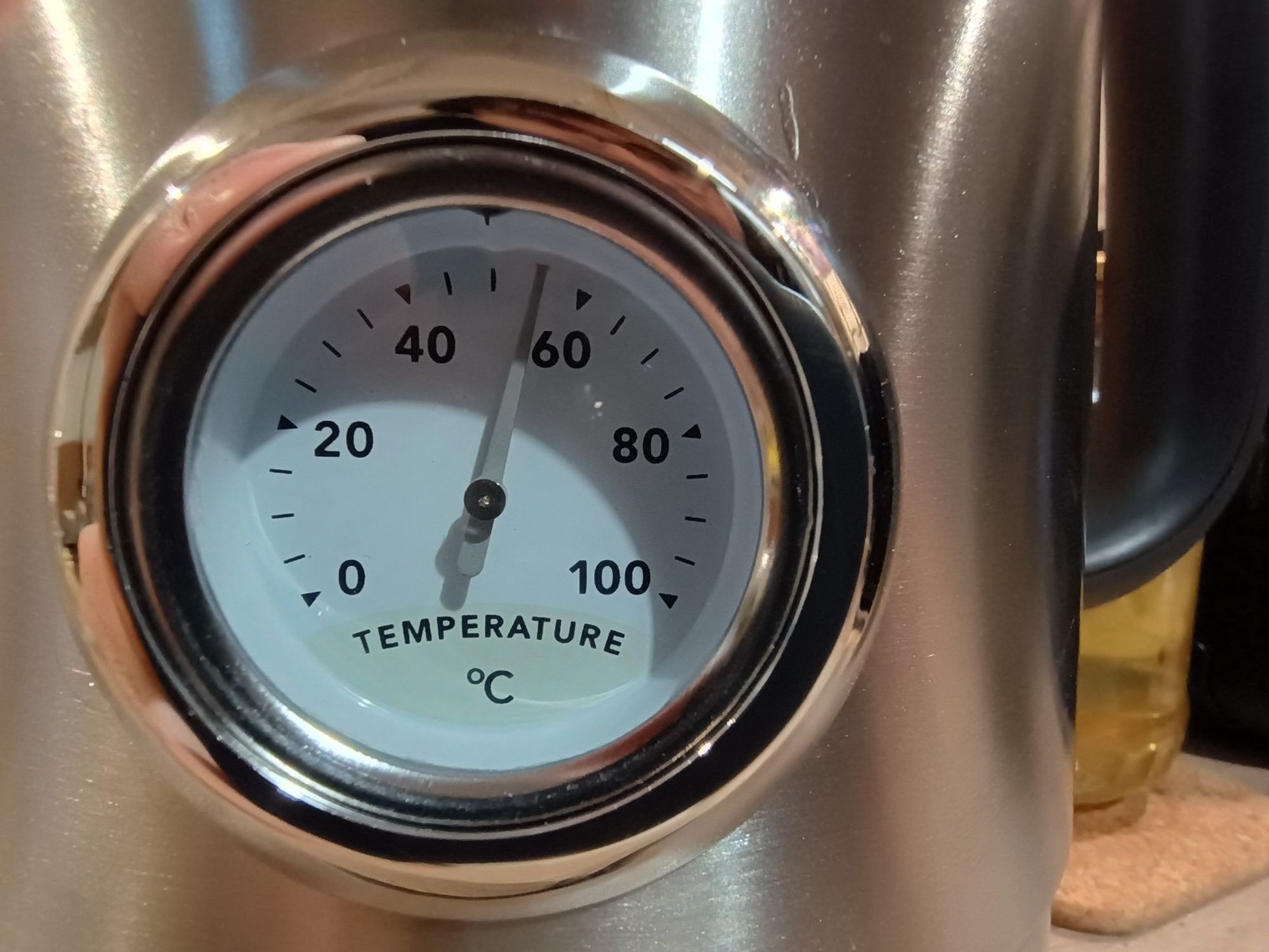 Closeup of the side of a stainless steel kettle with an analogue thermometer built in