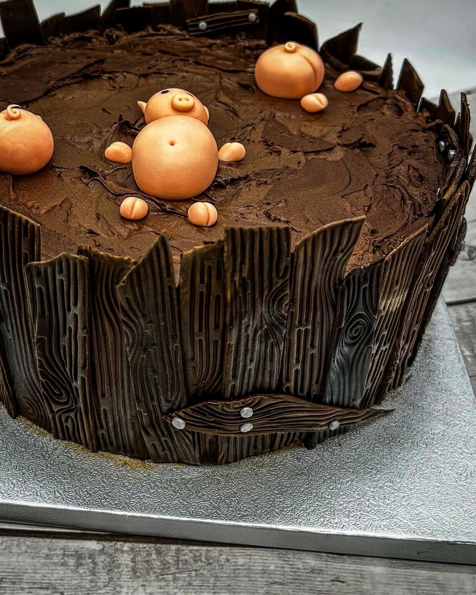 Eine braune Torte mit einem liegenden rosa Fondant Schwein darauf 
Neben dem liegenden Schwein sieht man noch zwei Schweine Poppes aus der Schoki gucken