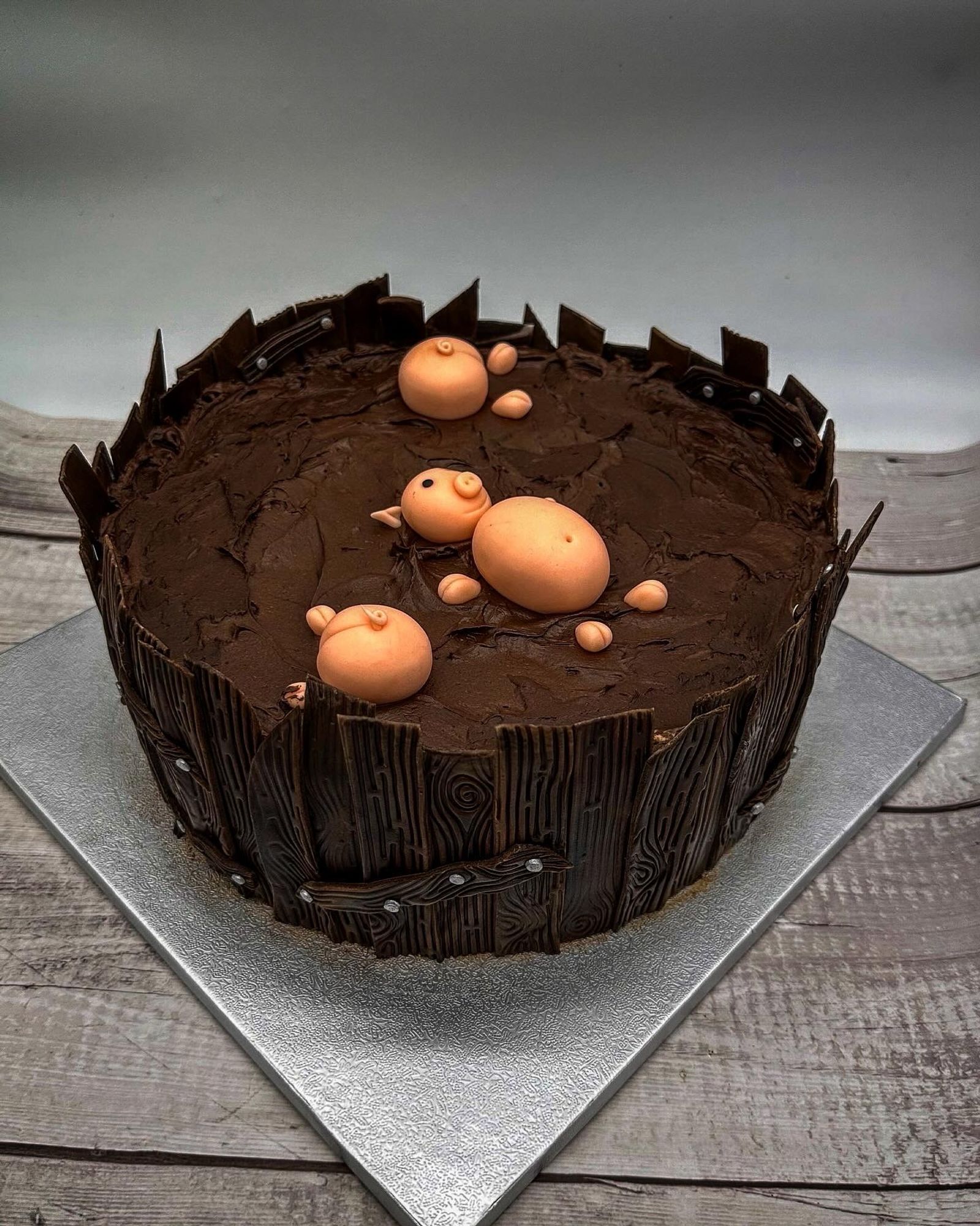 Eine braune Torte mit einem liegenden rosa Fondant Schwein darauf 
Neben dem liegenden Schwein sieht man noch zwei Schweine Poppes aus der Schoki gucken