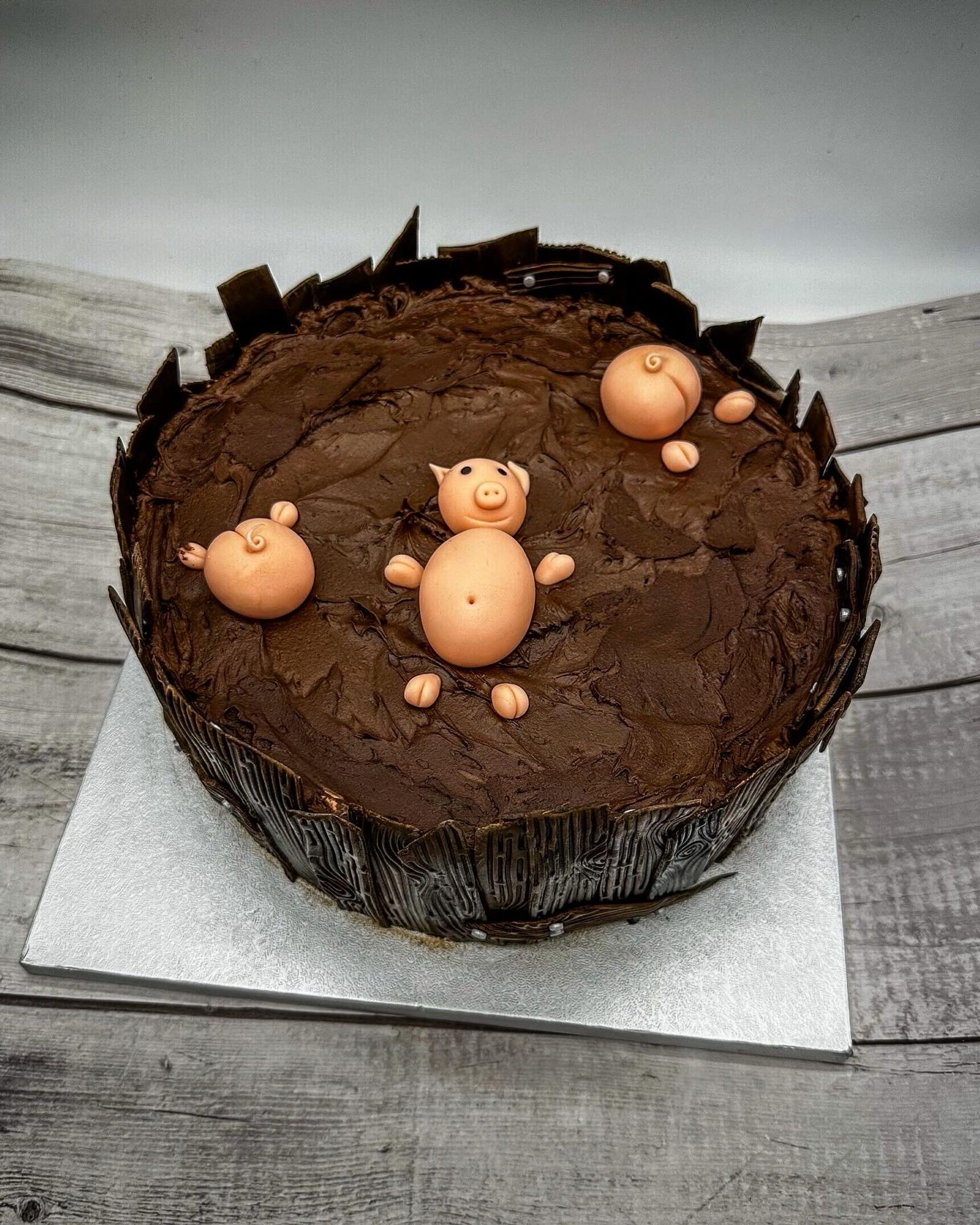 Eine braune Torte mit einem liegenden rosa Fondant Schwein darauf 
Neben dem liegenden Schwein sieht man noch zwei Schweine Poppes aus der Schoki gucken