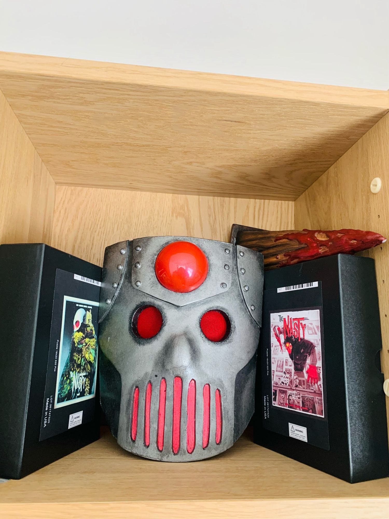 A bookshelf featuring a replica Red Ennis mask and railroad spike, plus some The Nasty puzzle sets.