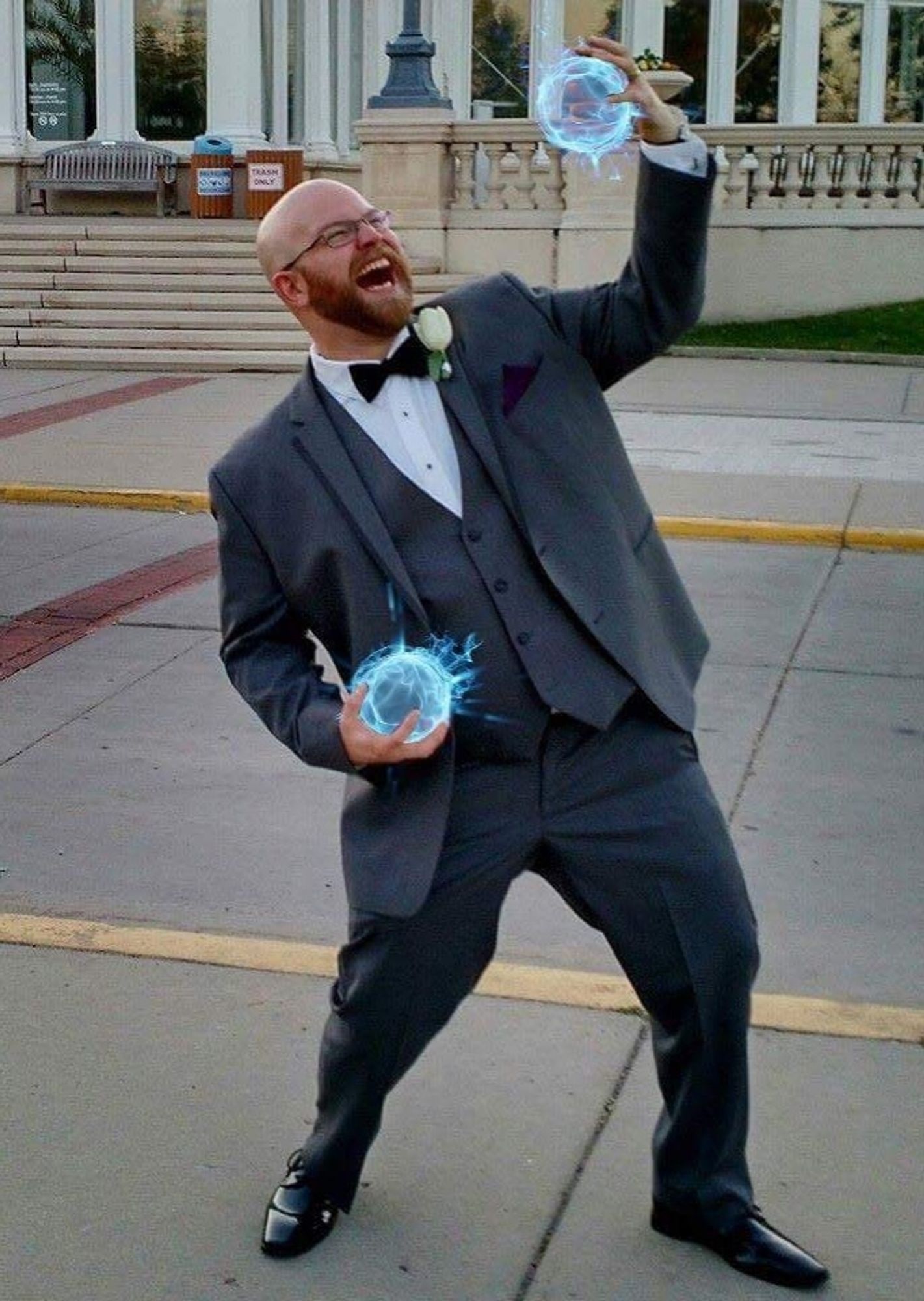 Bearded person in a gray tuxedo with blue energy balls in hands