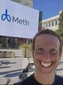 Mark Zuckerberg, wide smiled, standing infront of the meta logo that has been edited to say “meth” and the icon changed to a penile shape.