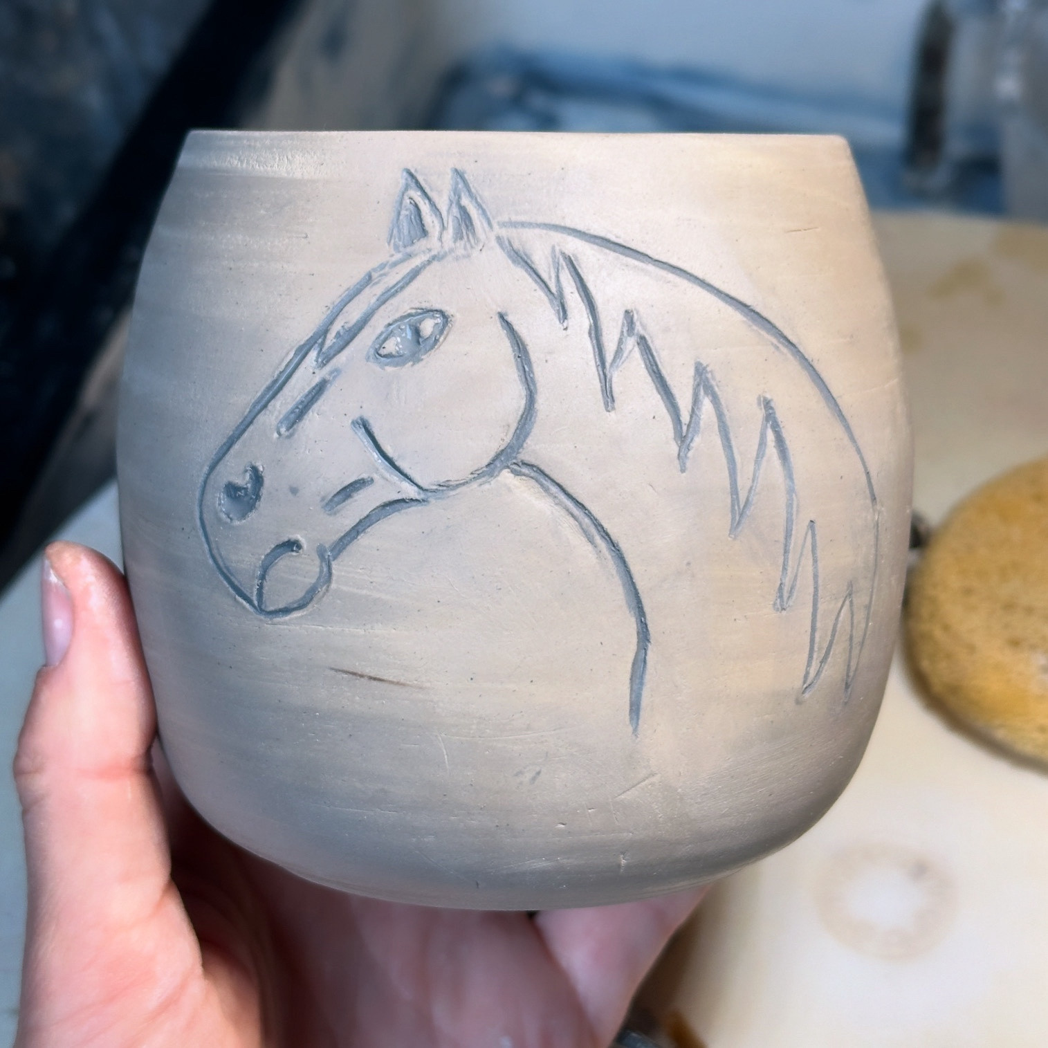 A clay pottery mug with the outline of a horse from the neck up giving serious side eye. 