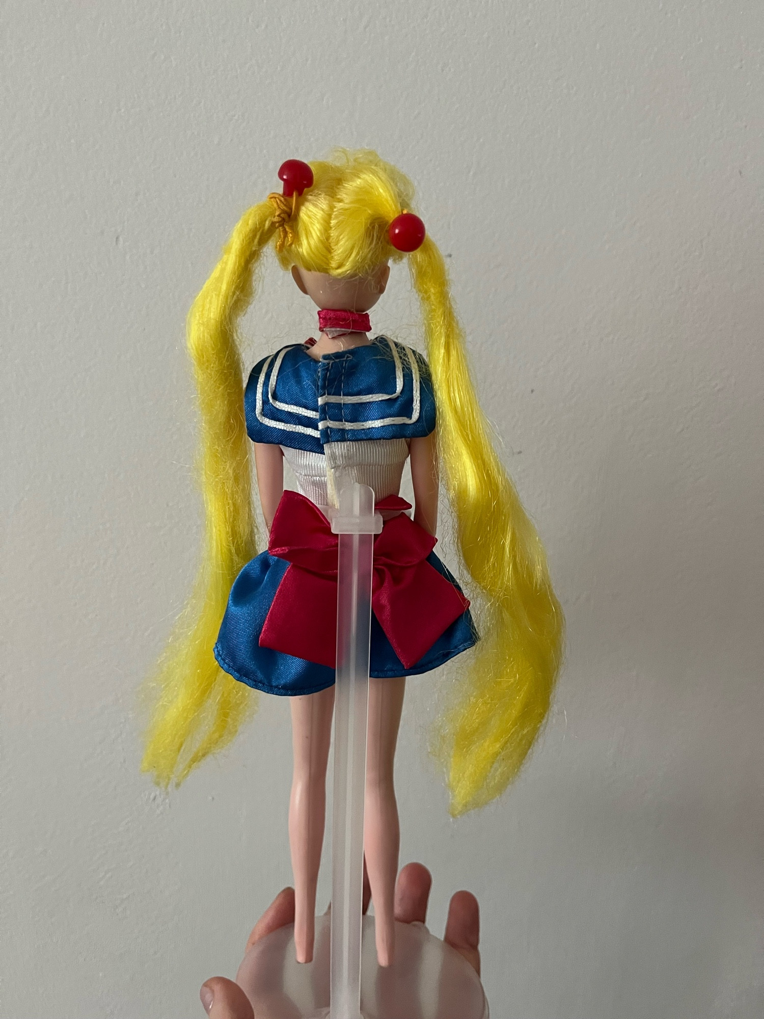 Boneca Sailor Moon com longos cabelos loiros vista de costas, com uniforme de marinheira e um laço vermelho enorme atrás