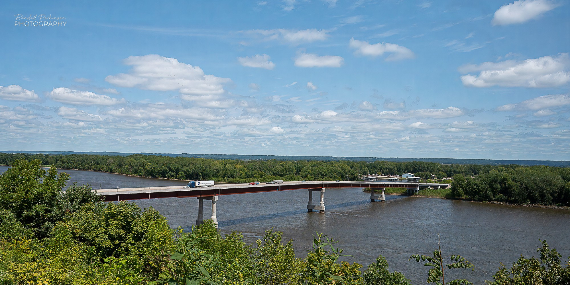 A two lane steel plate girder bridge crossing the Mississippi River on a sunny day with a few white clouds.