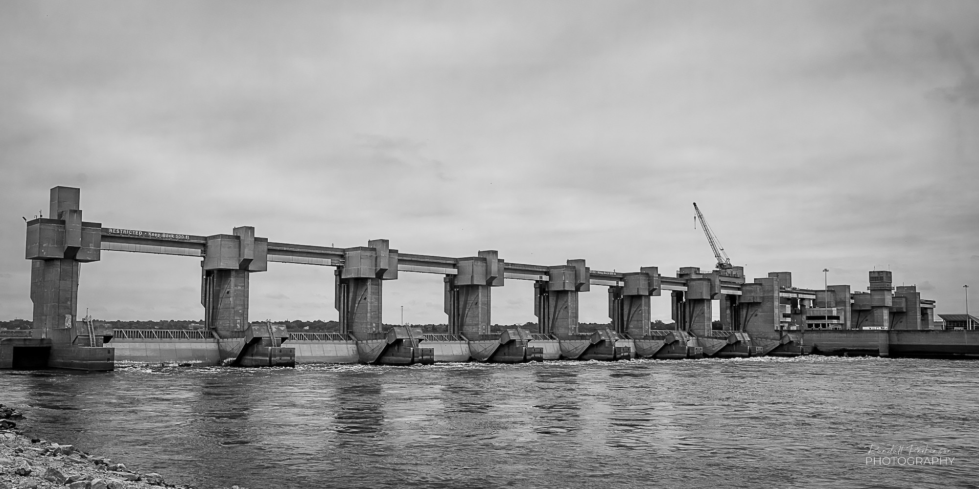 A view of a large concrete dam across the Mississippi River taken from the riverbank just below the dam.