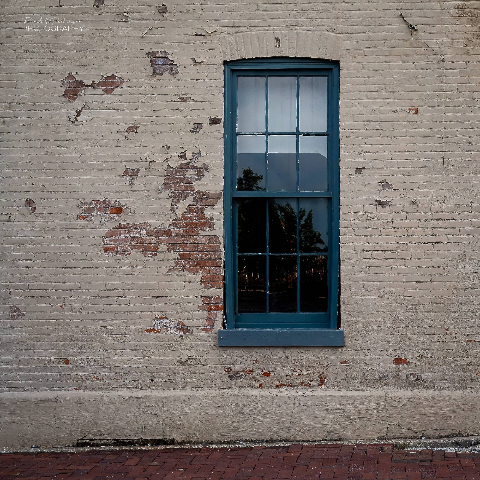 A tall green framed window set in a bridge wall with peeling tan paint.