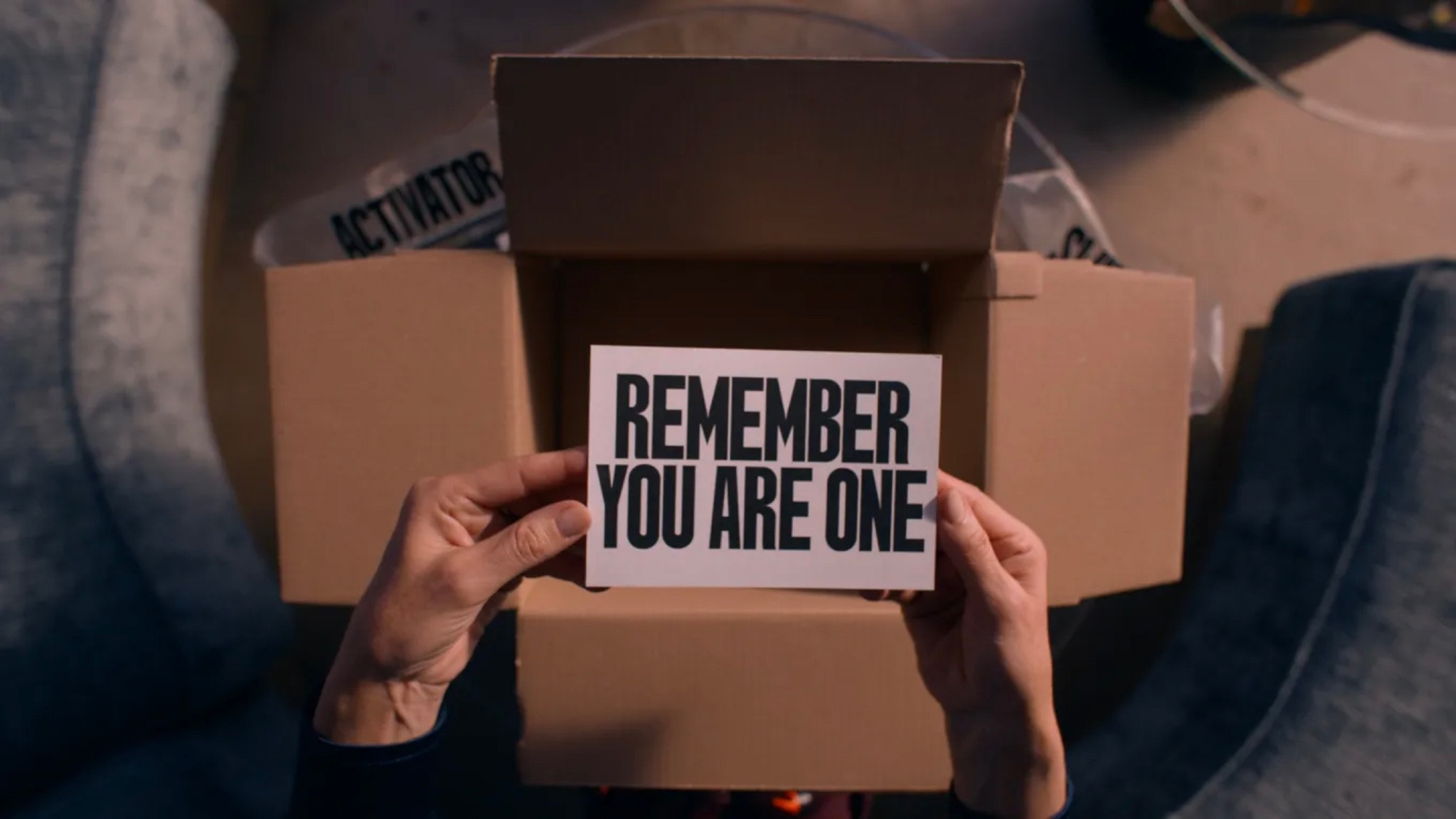 Una imagen de la película La sustancia: dos manos sujetan una tarjeta blanca de gran tamaño sacada de una caja en la que se puede leer el texto: REMEMBER YOU ARE ONE.