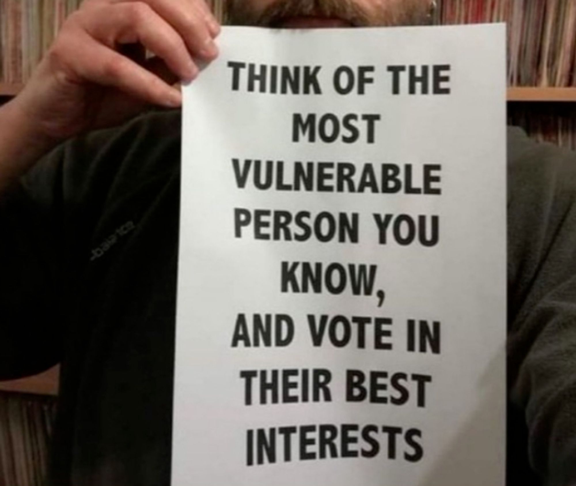 man holding sign that reads: "think of the most vulnerable person you know, and vote in their best interests"