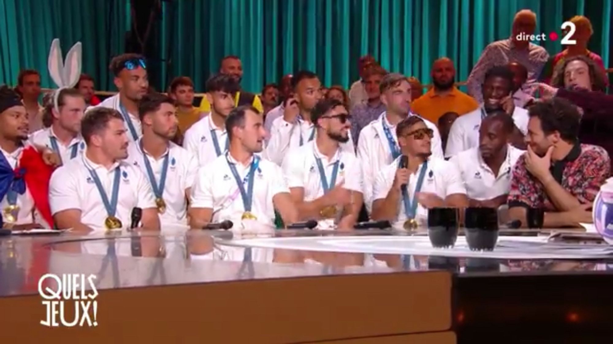 Rugbymen de l’équipe de rugby à 7 championne olympique, alignés derrière une table sur le plateau de « Quels jeux » sur France 2