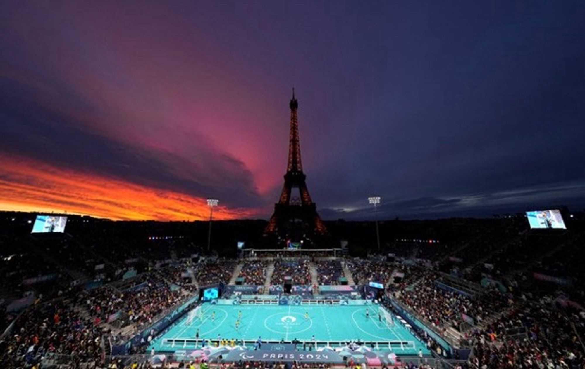 Terrain de cécifoot aux pieds de la Tour Eiffel, crépuscule jaune, orange, rose, bleu nuit