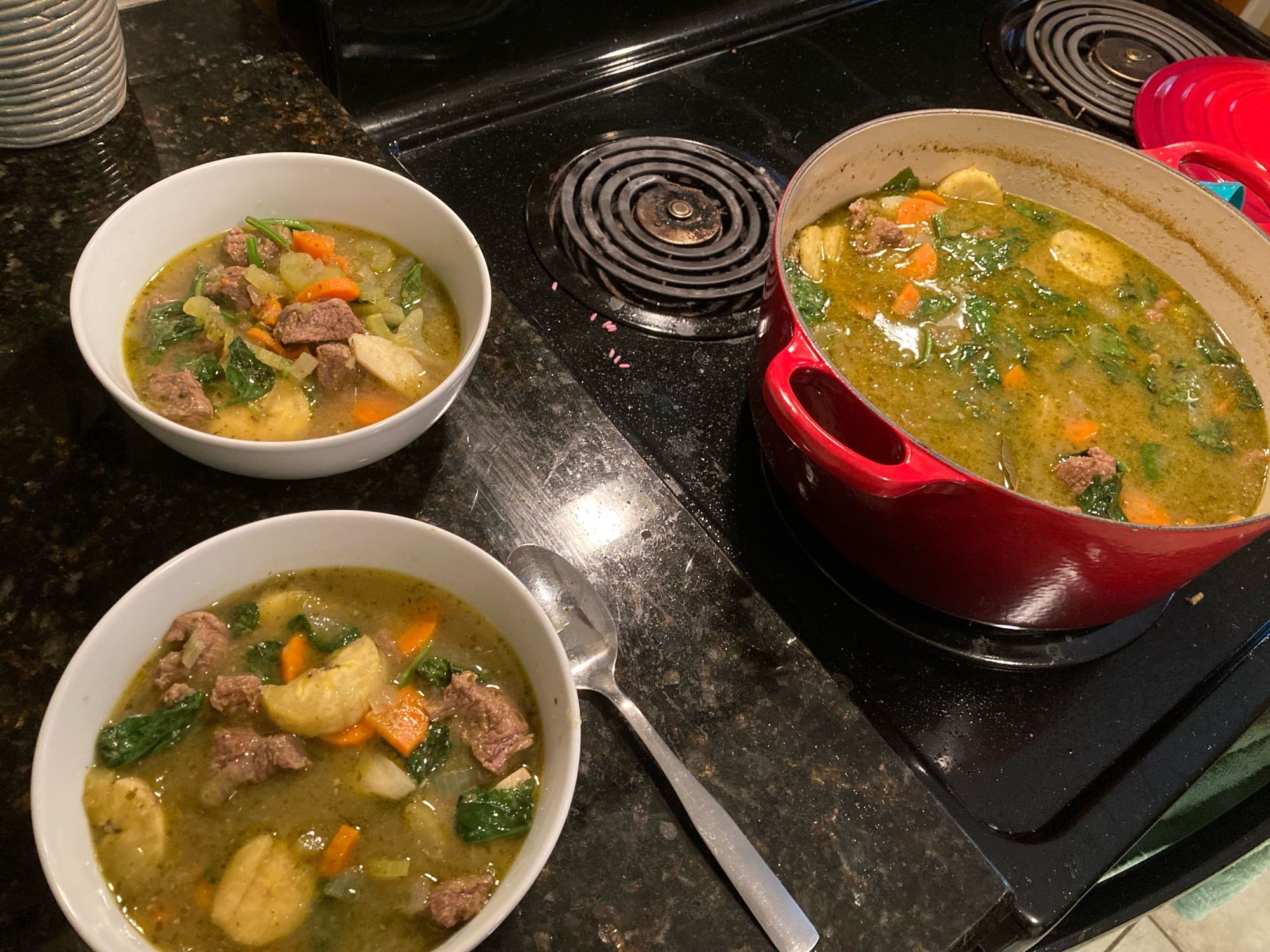 Two bowls full of bouyon bef next to a dutch oven full of bouyon bef.