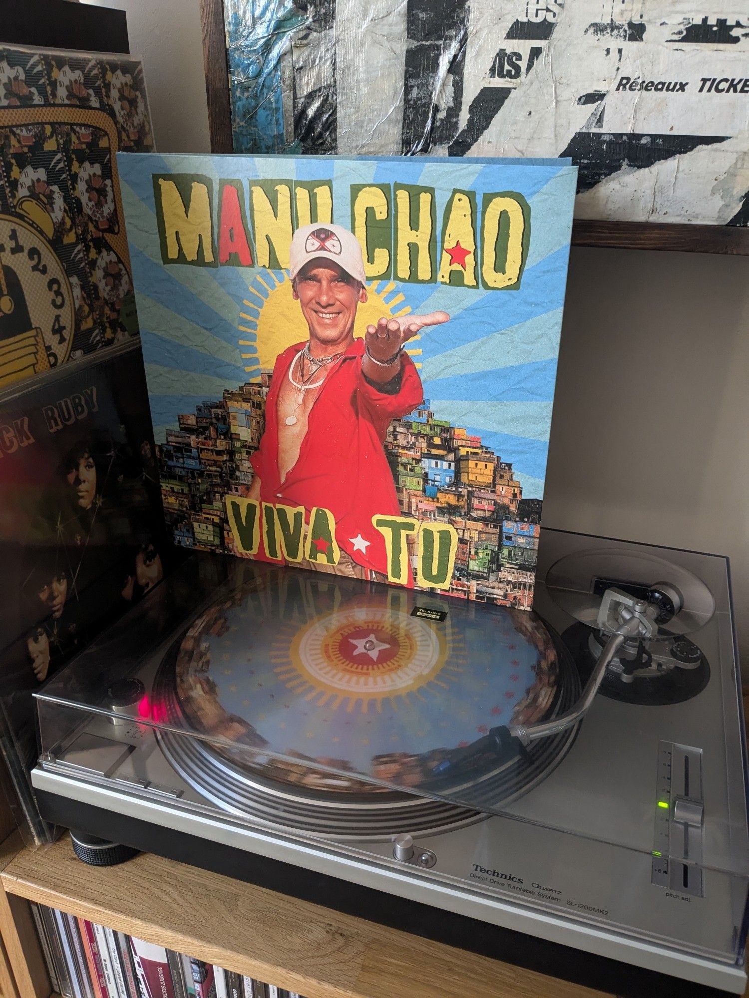 Pochette vinyle de Viva Tu, dernier album de Manu Chao. Il nous tend la main en souriant sur la photo.

Le disque est illustré, bleu avec des maisons sur la périphérie